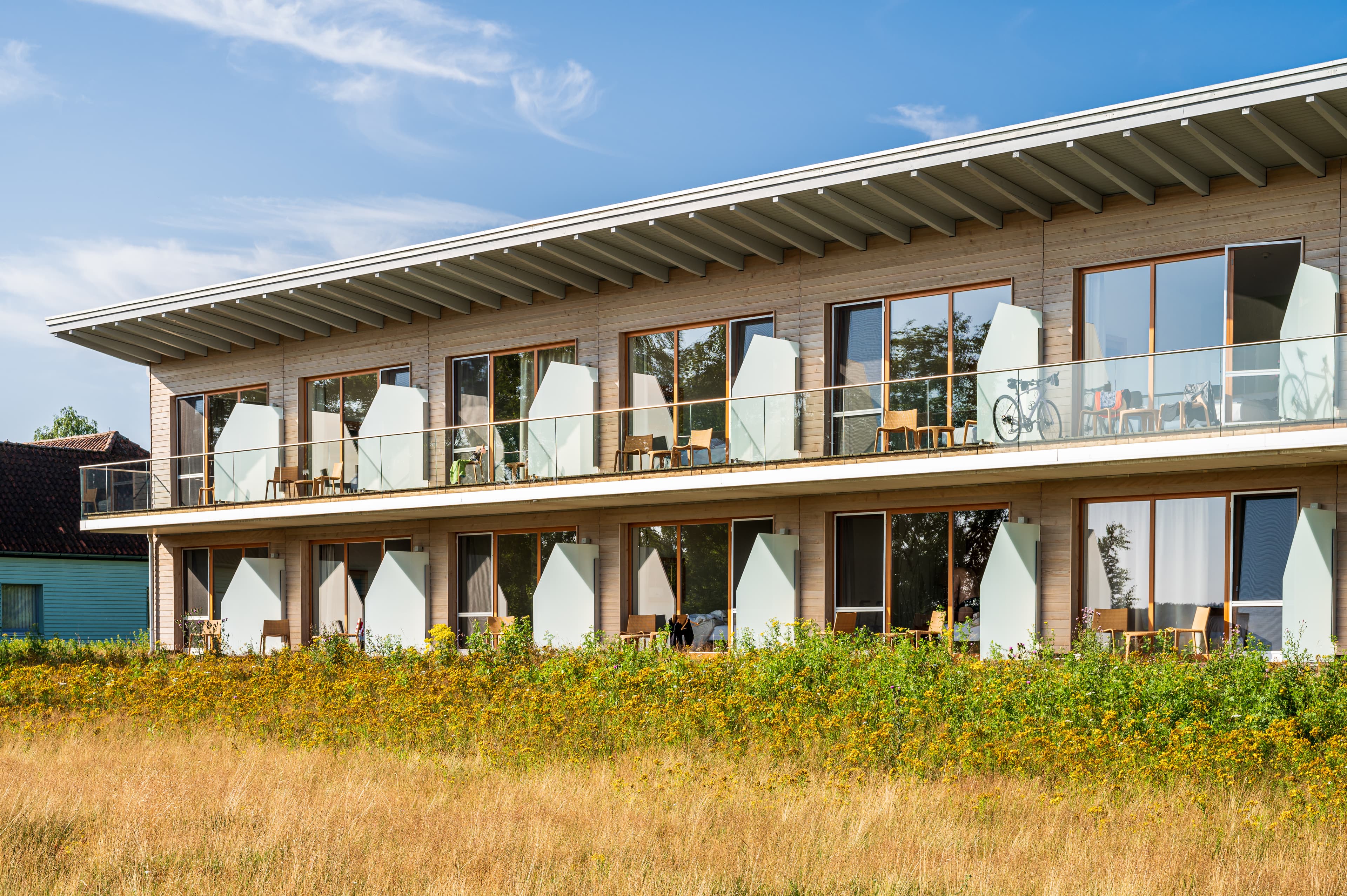 Außenansicht von zweistöckigen Hotelzimmern mit Terrasse und Ausblick ins Grüne.