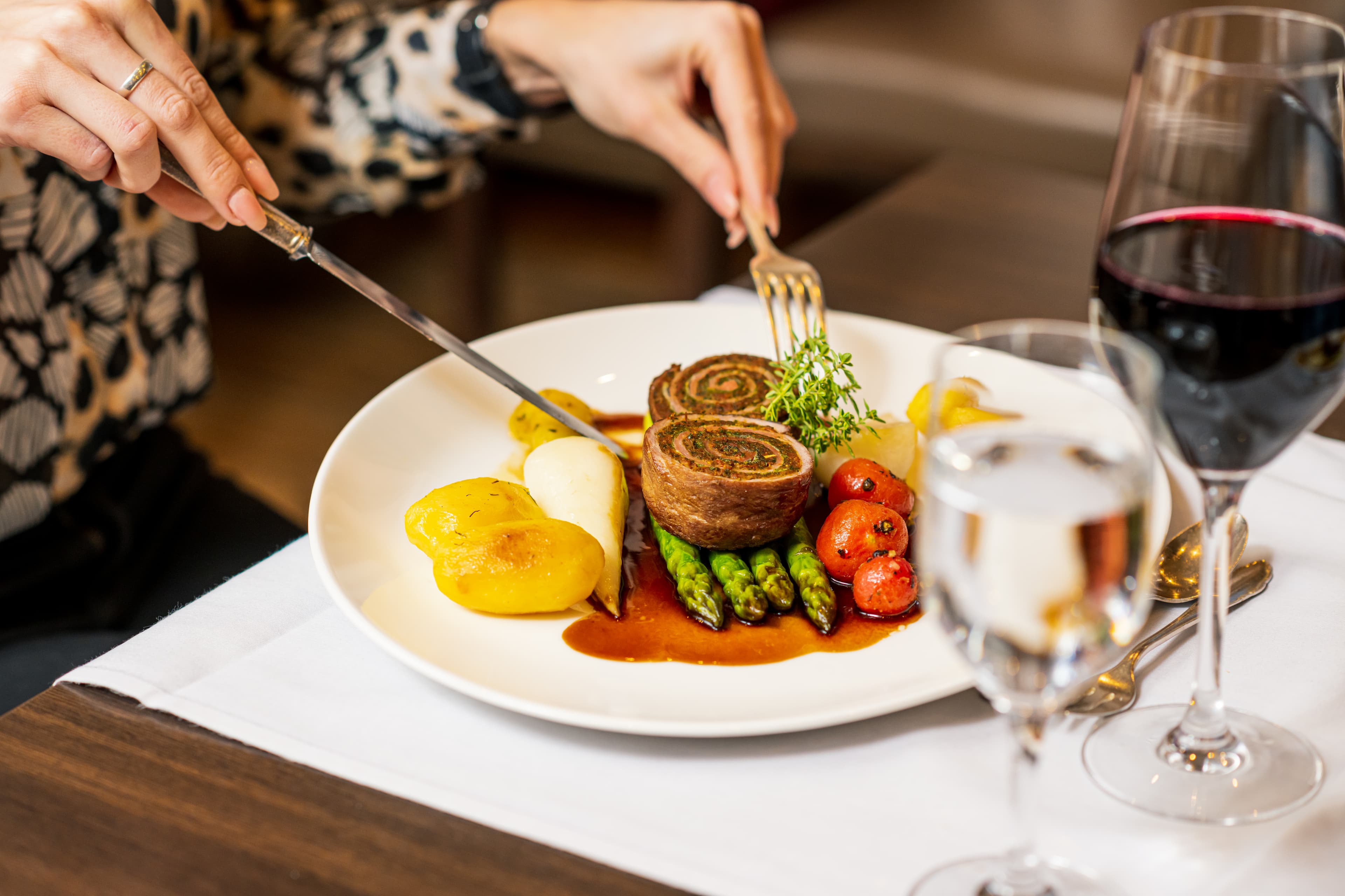 GEfüllter Teller mit Spargel, Sauce, Fleisch und einer Frau, die gerade anfängt zu essen.
