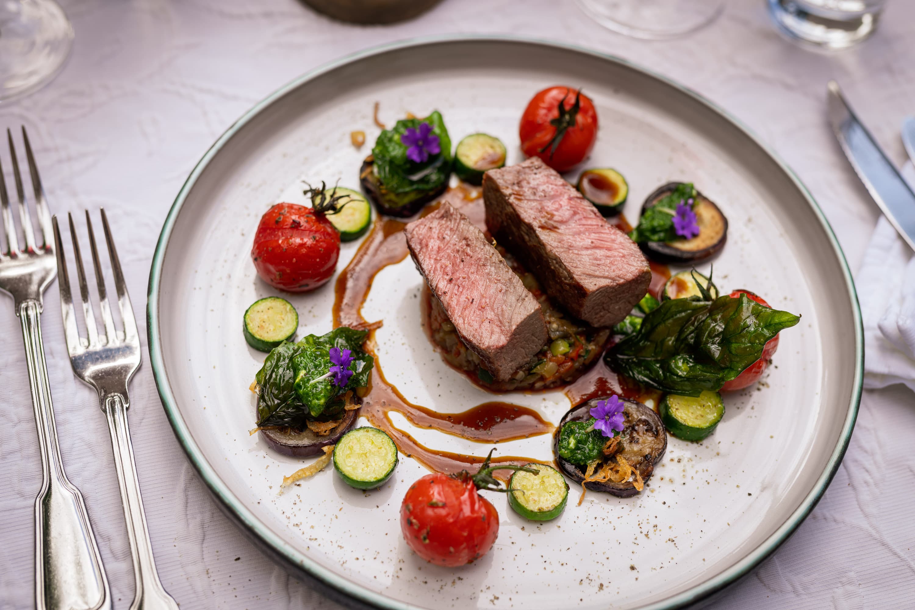 Angerichtetes Heidschnucken Filet, rosa gebraten, mit mediterranem Gemüse und Soße auf Teller.