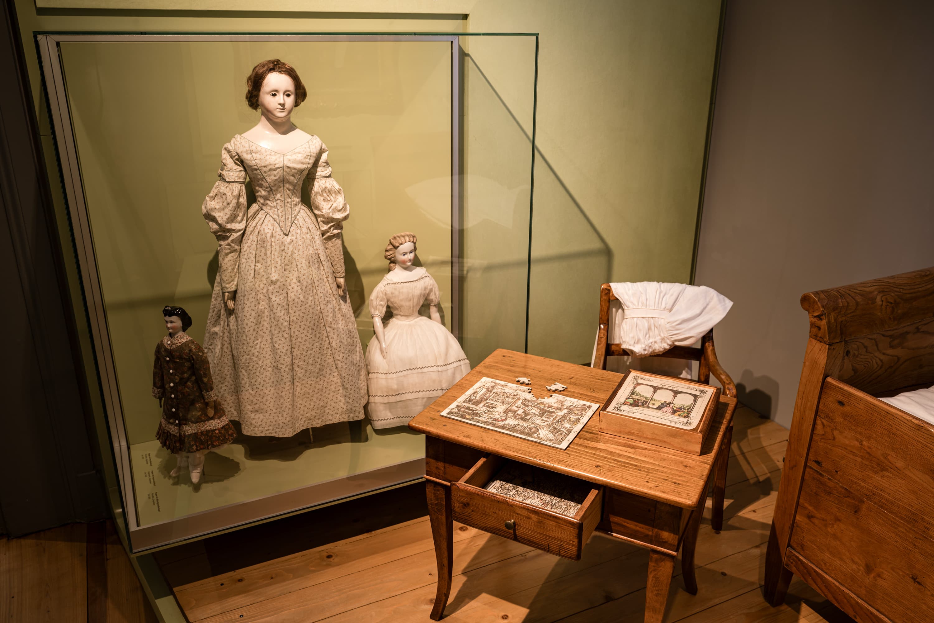 Historisches Kinderzimmer mit alten Puppen in einer Vitrine und einem Holztisch mit Puzzle.