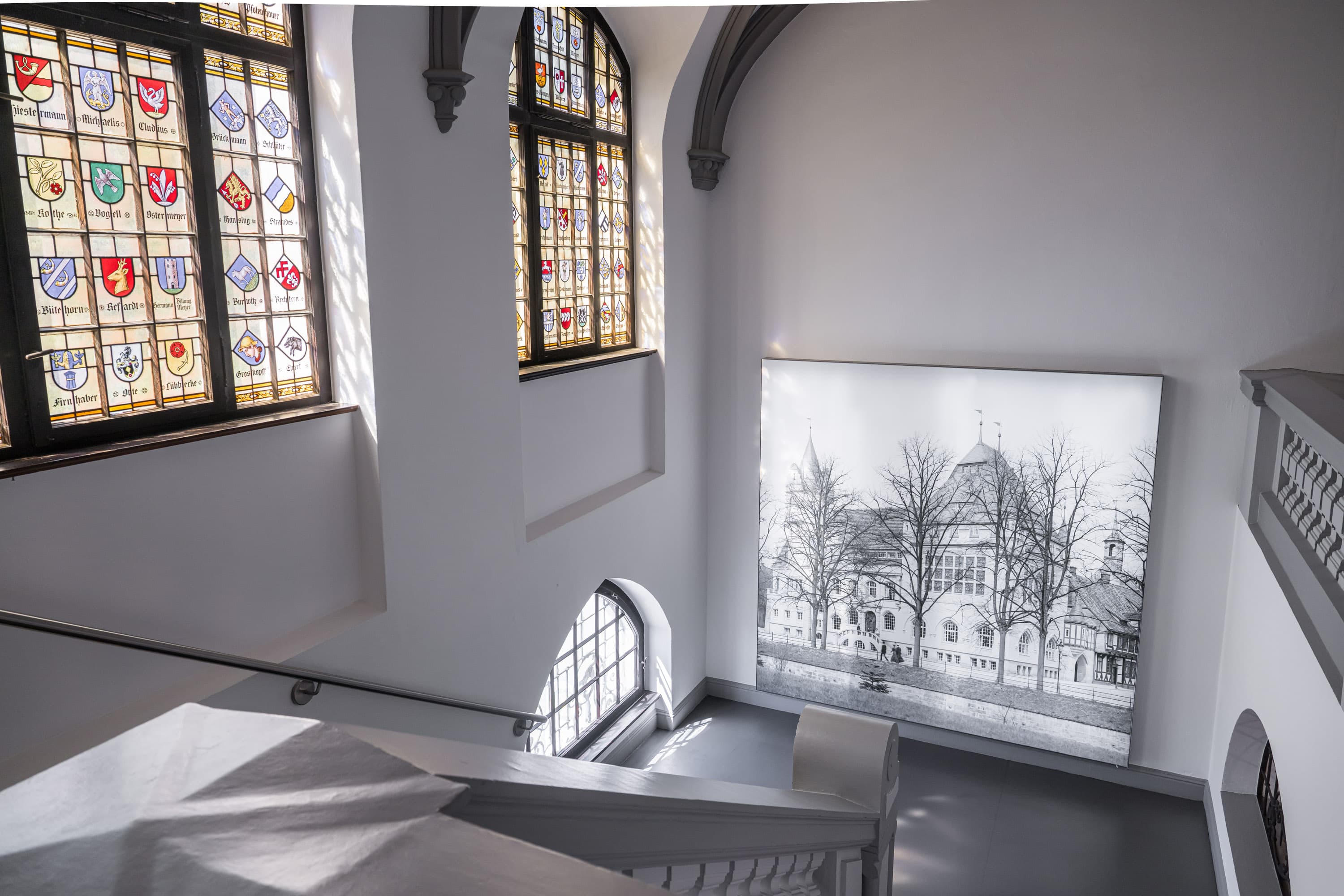 Helles Treppenhaus im Bomann-Museum Celle mit Buntglasfenstern und einer großen historischen Fotografie.
