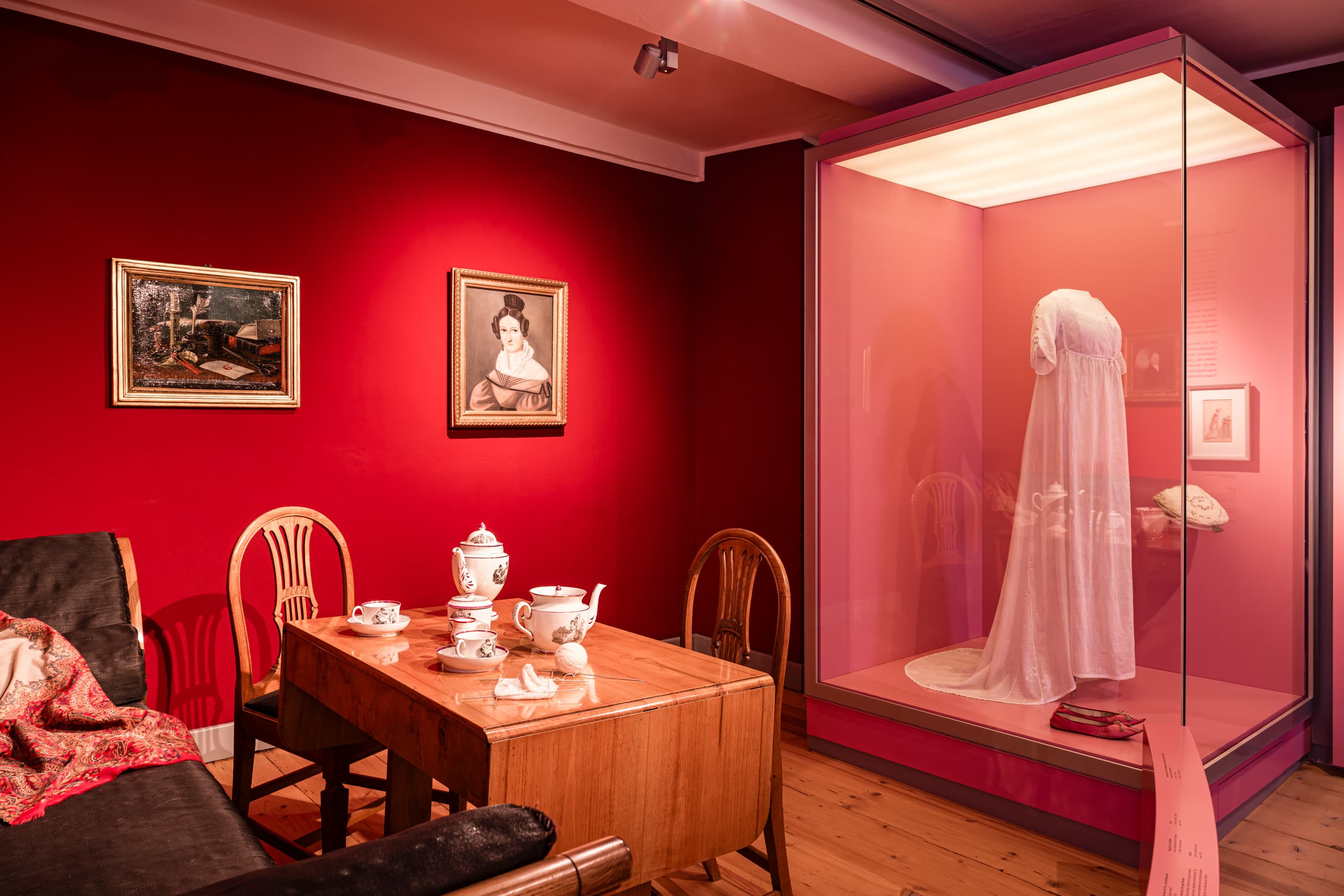 Ausstellungsraum im Bomann-Museum mit roten Wänden, gedecktem Tisch und einem Kleid in einer Vitrine.