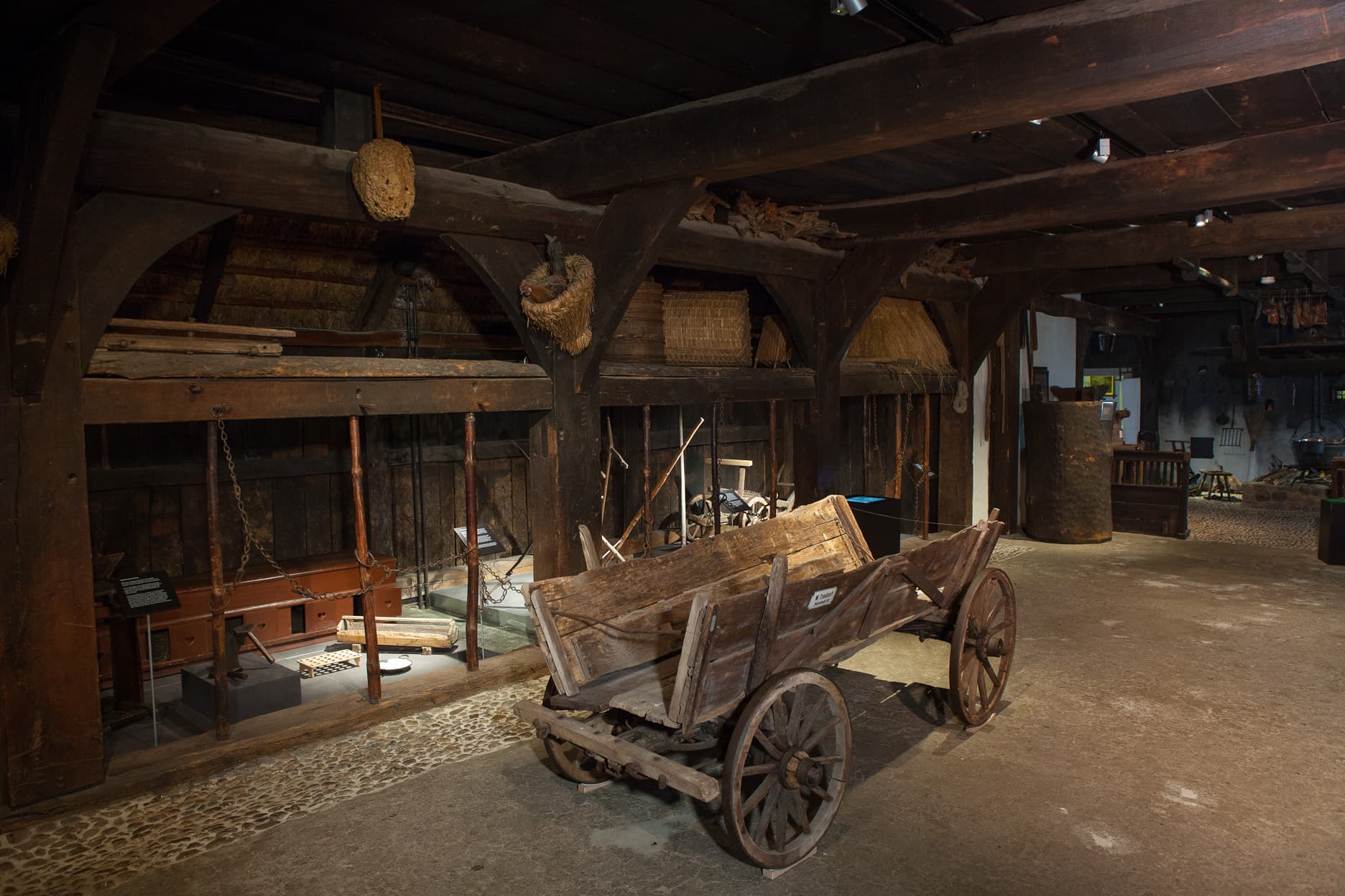 Einblick in das frühere Landleben: Diele eines Bauernhauses mit Holzwagen unter schweren Deckenbalken.