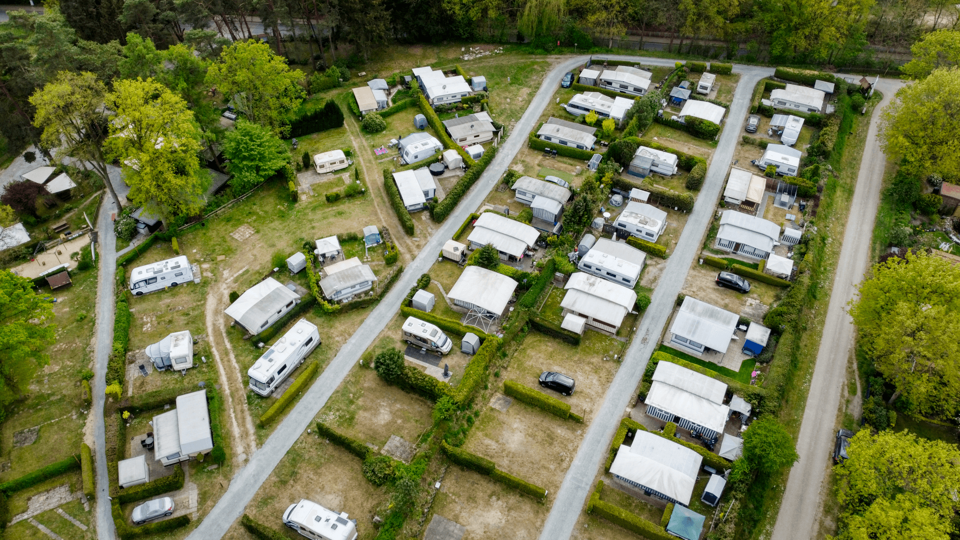 Luftaufnahme eines gepflegten Campingplatzes mit Wohnwagen und Mobilheimen in grüner Umgebung. Schmale Wege führen zwischen den Parzellen hindurch, umgeben von Hecken und Bäumen. Der Platz wirkt geordnet und ruhig, eingebettet in eine von Wäldern und Wiesen geprägte Landschaft des Lopautals.