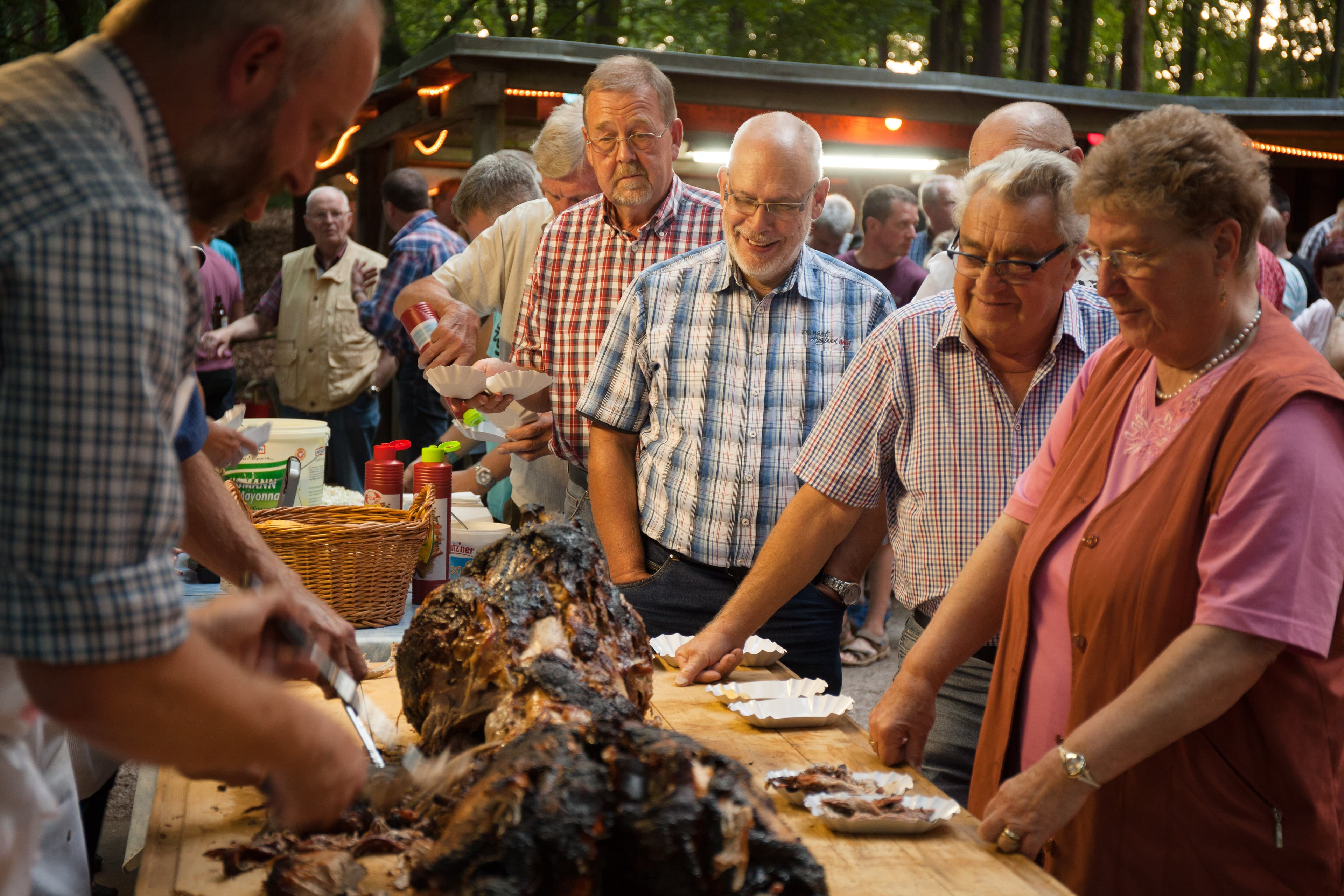 Menschen servieren und teilen Spanferkel bei einem traditionellen Dorffest auf dem Grillplatz in Volkwardingen.