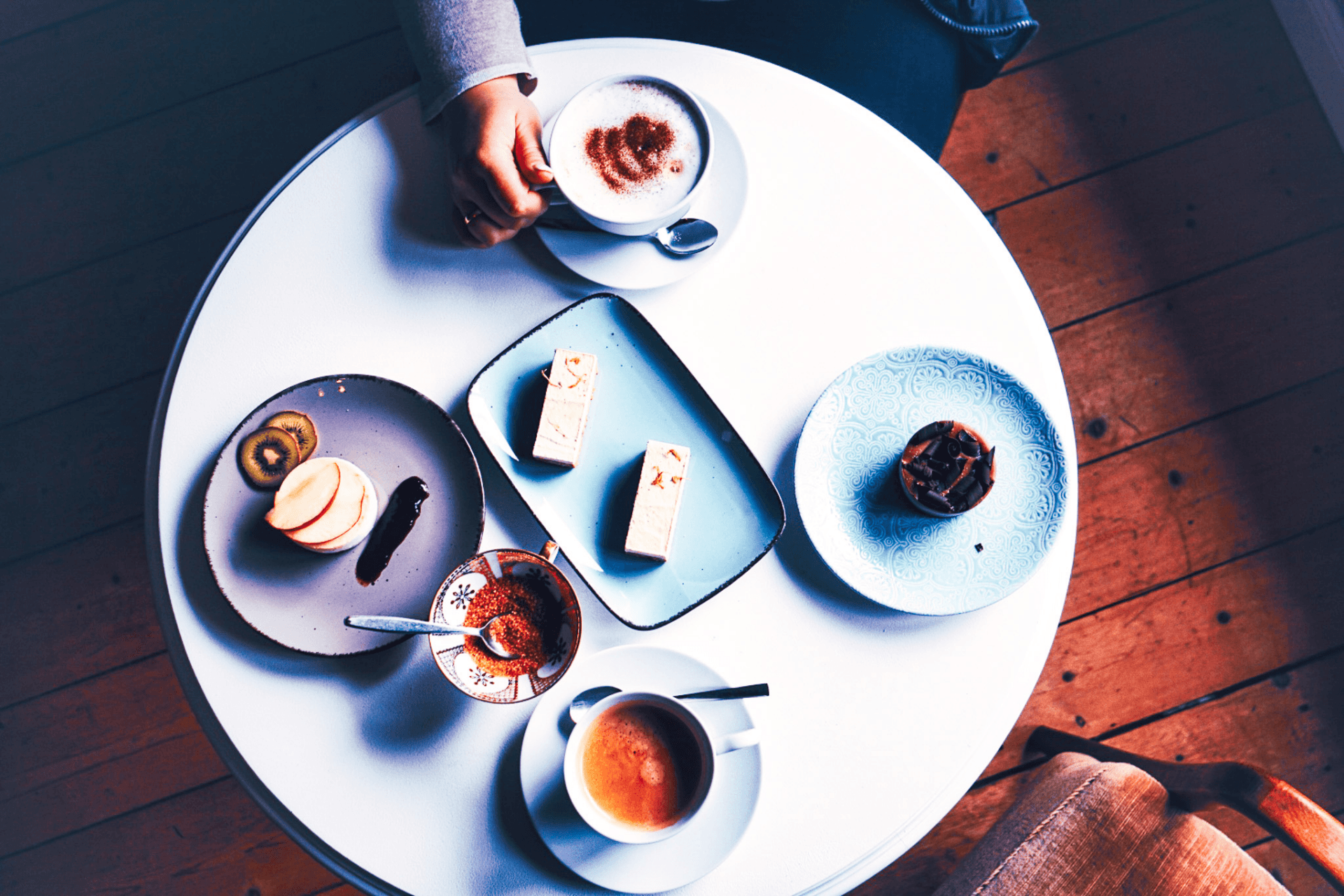 Weißer runder Tisch aus der Vogelperspektive mit Kaffee, Kuchenstücken und Törtchen auf Tellern.