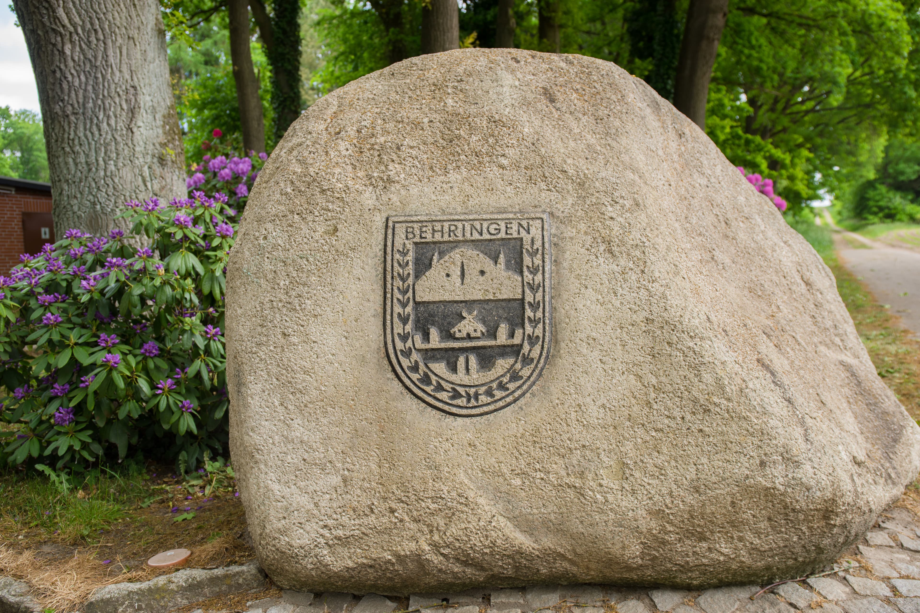 Ein großer Findling mit dem Wappen von Behringen, umgeben von Bäumen und Rhododendren.