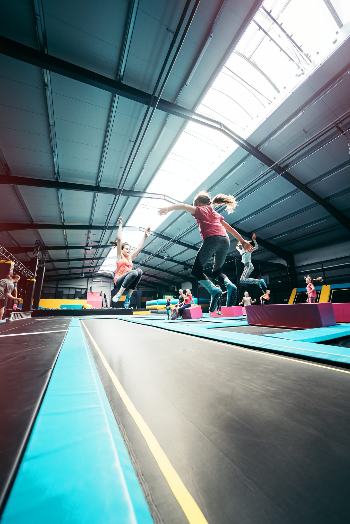 Mehrere Personen springen auf parallel angeordneten Trampolinen in einer hellen Halle.