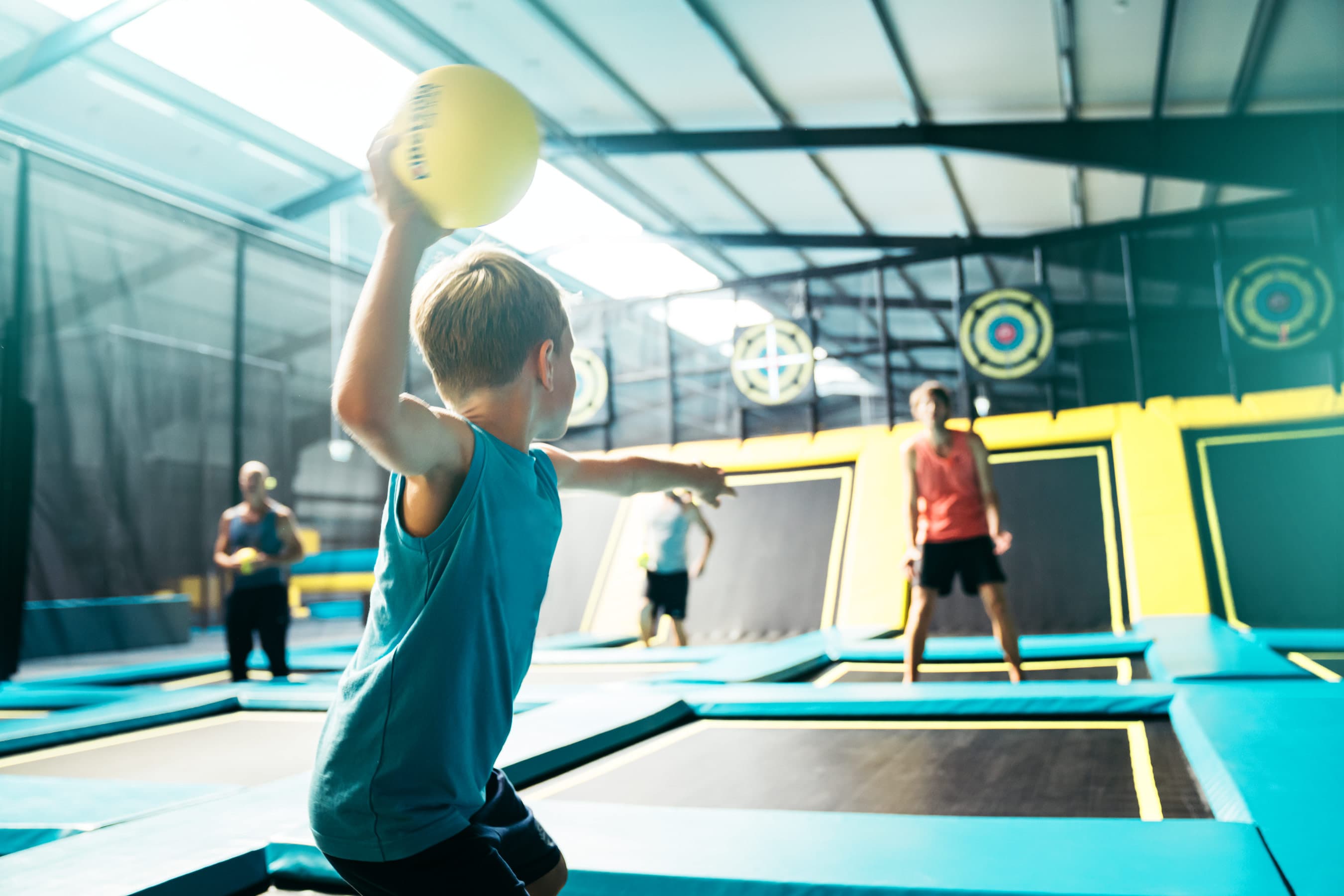 Junge beim Werfen eines Balls auf einem Trampolin in einer Abenteuerspiel- und Trampolinhalle.