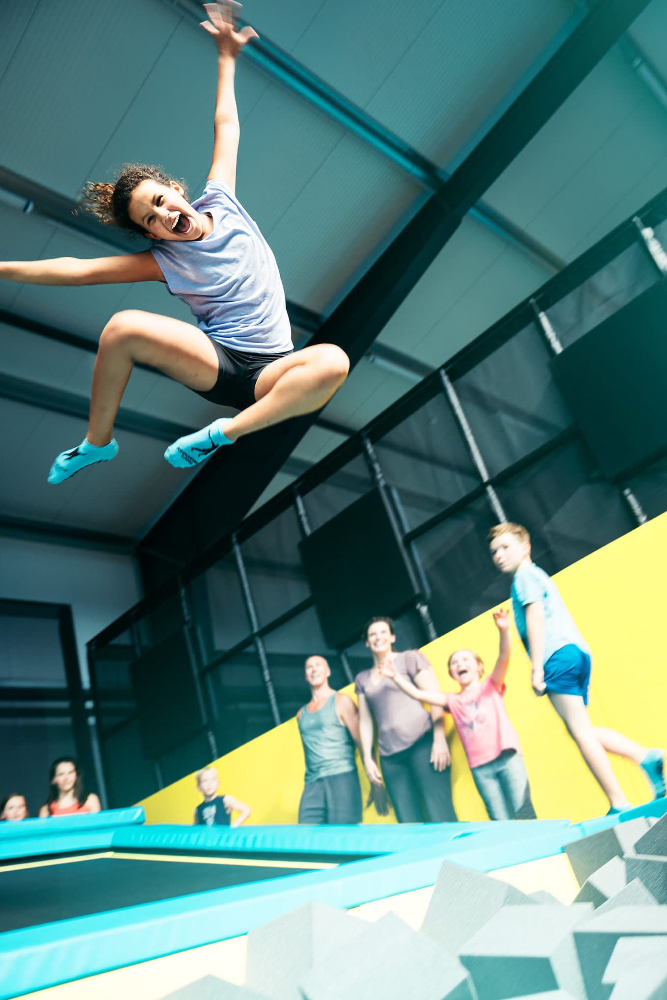 Eine Frau springt freudestrahlend auf einem Trampolin, während im Hintergrund mehrere Personen zusehen.