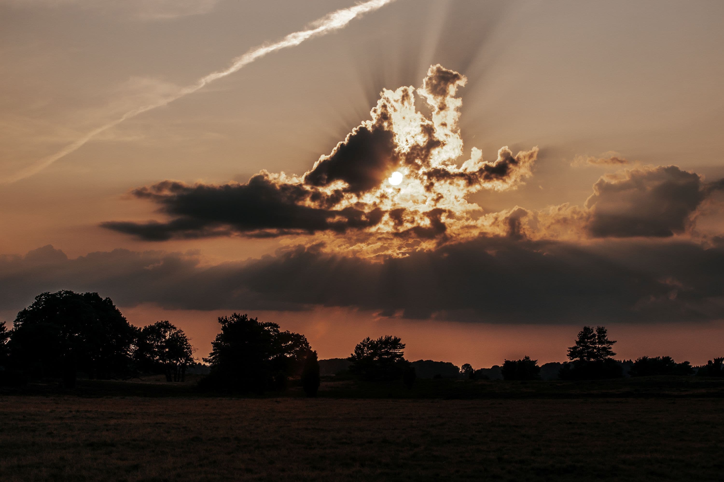 Die untergehende Sonne leuchtet hinter den Schleierwolken hervor