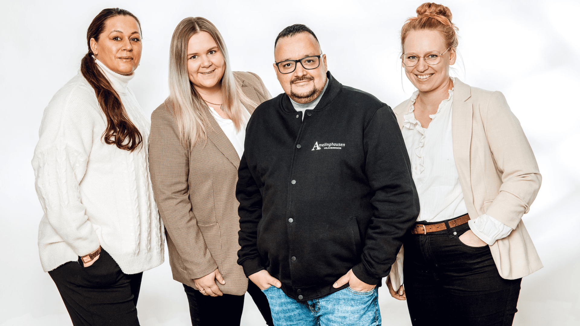 Vier freundlich lächelnde Menschen in Business-Kleidung vor weißem Hintergrund.