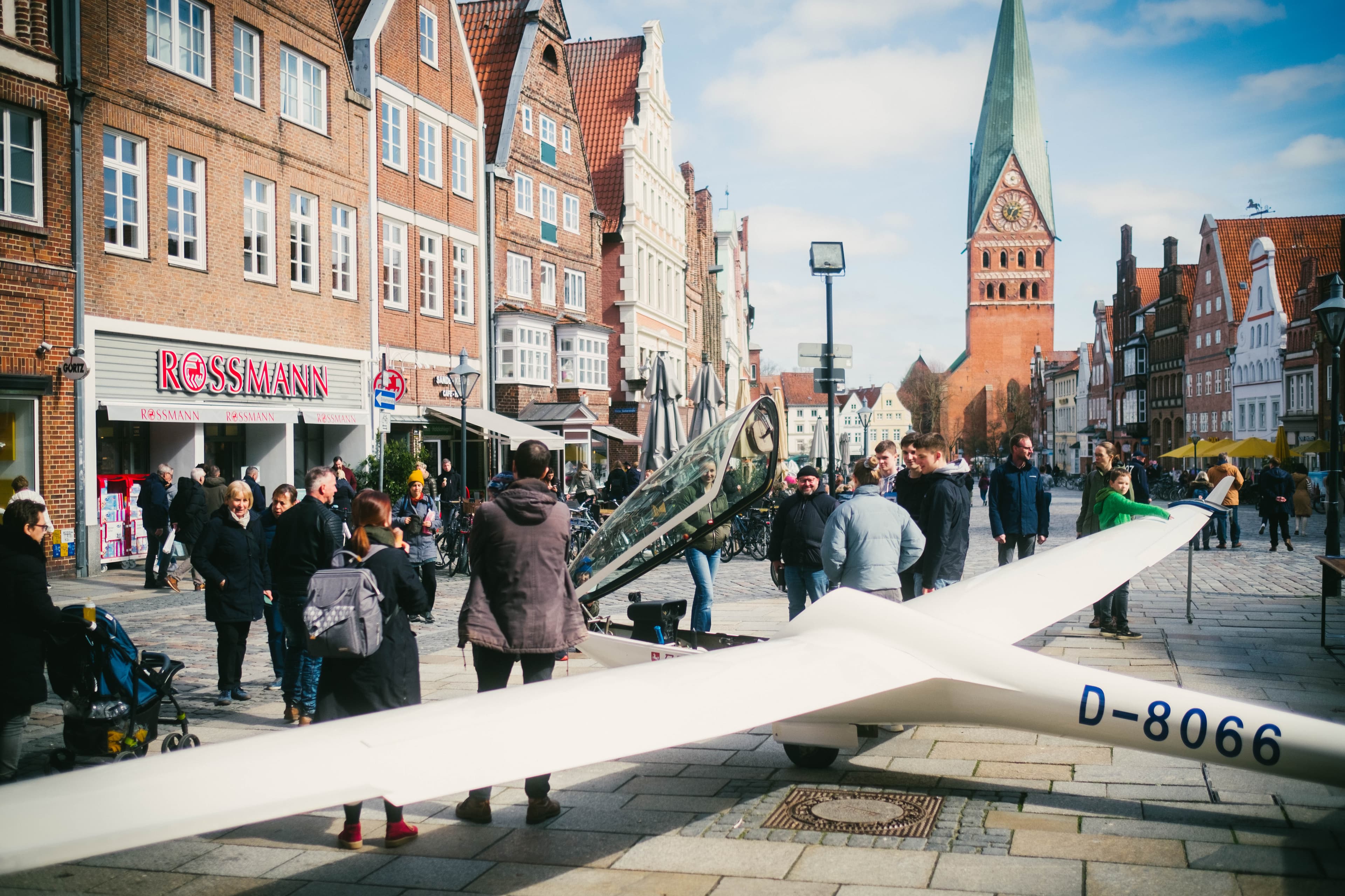 Menschen betrachten ein weißes Segelflugzeug in der historischen Fußgängerzone von Lüneburg.