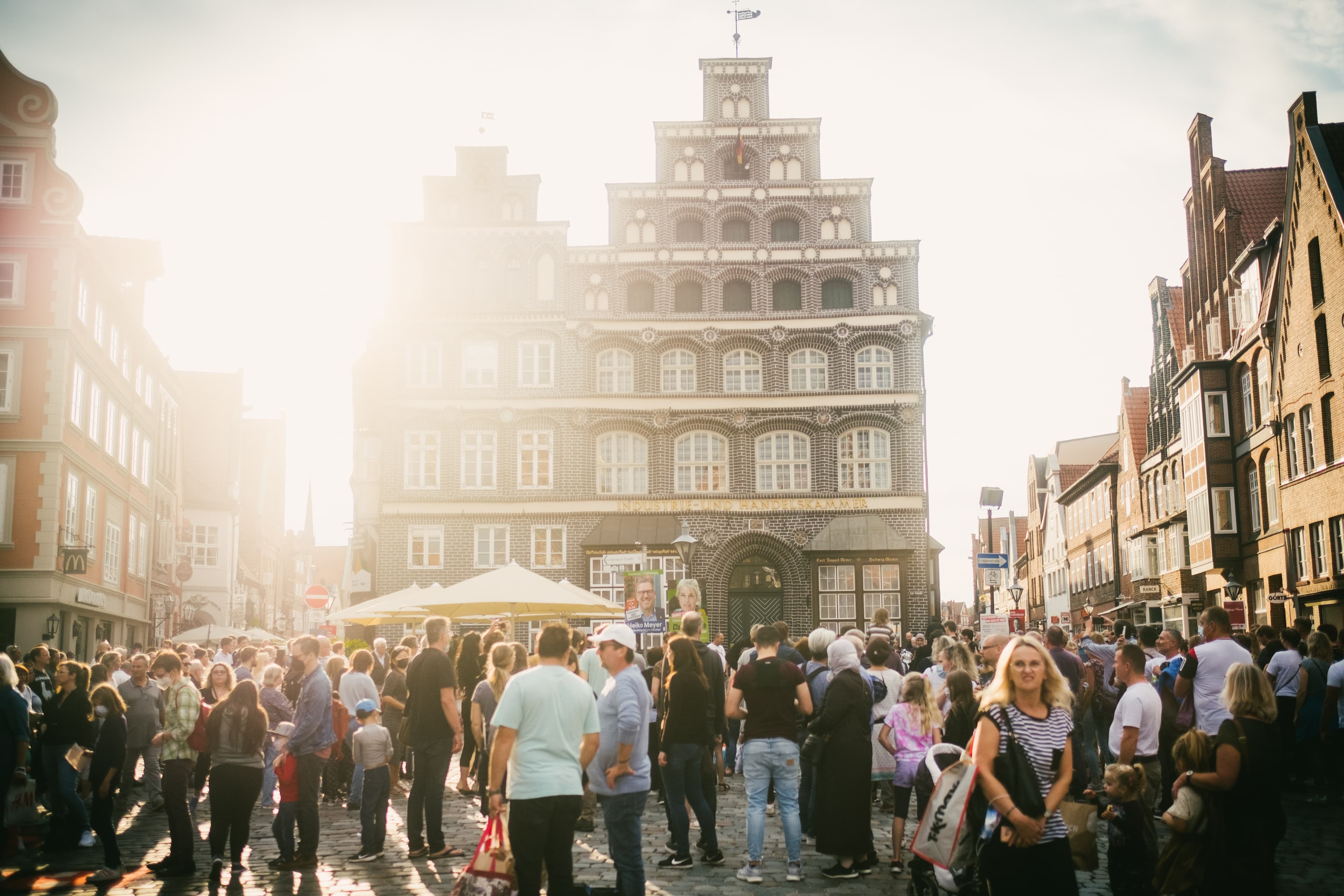 Zuschauermenge beim Tag der Straßenmusik vor dem historischen IHK-Gebäude in Lüneburg im Sonnenlicht.