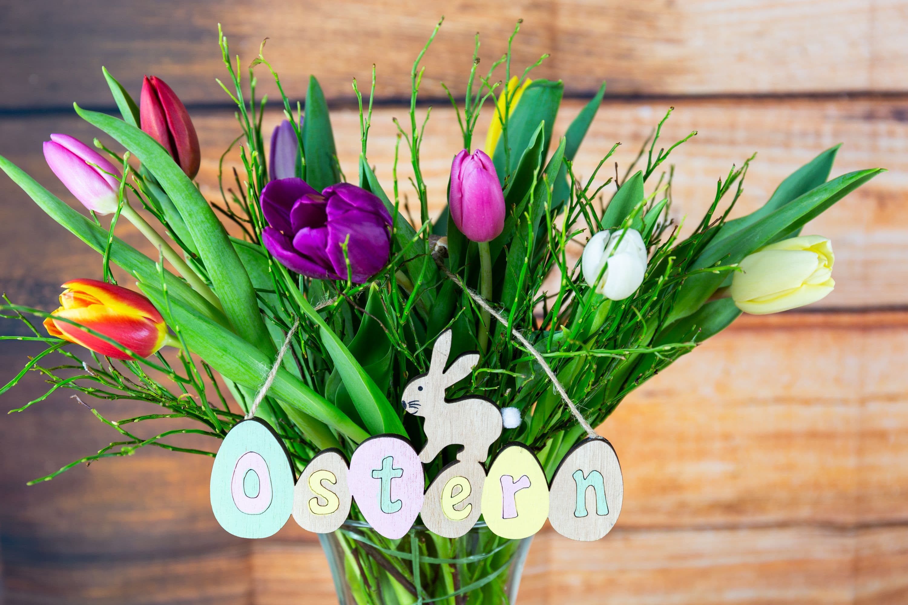 ein bunter strauß blumen mit tulpen in lila und gelb steht auf einem tisch zusammen mit einem schild auf dem steht frohe ostern