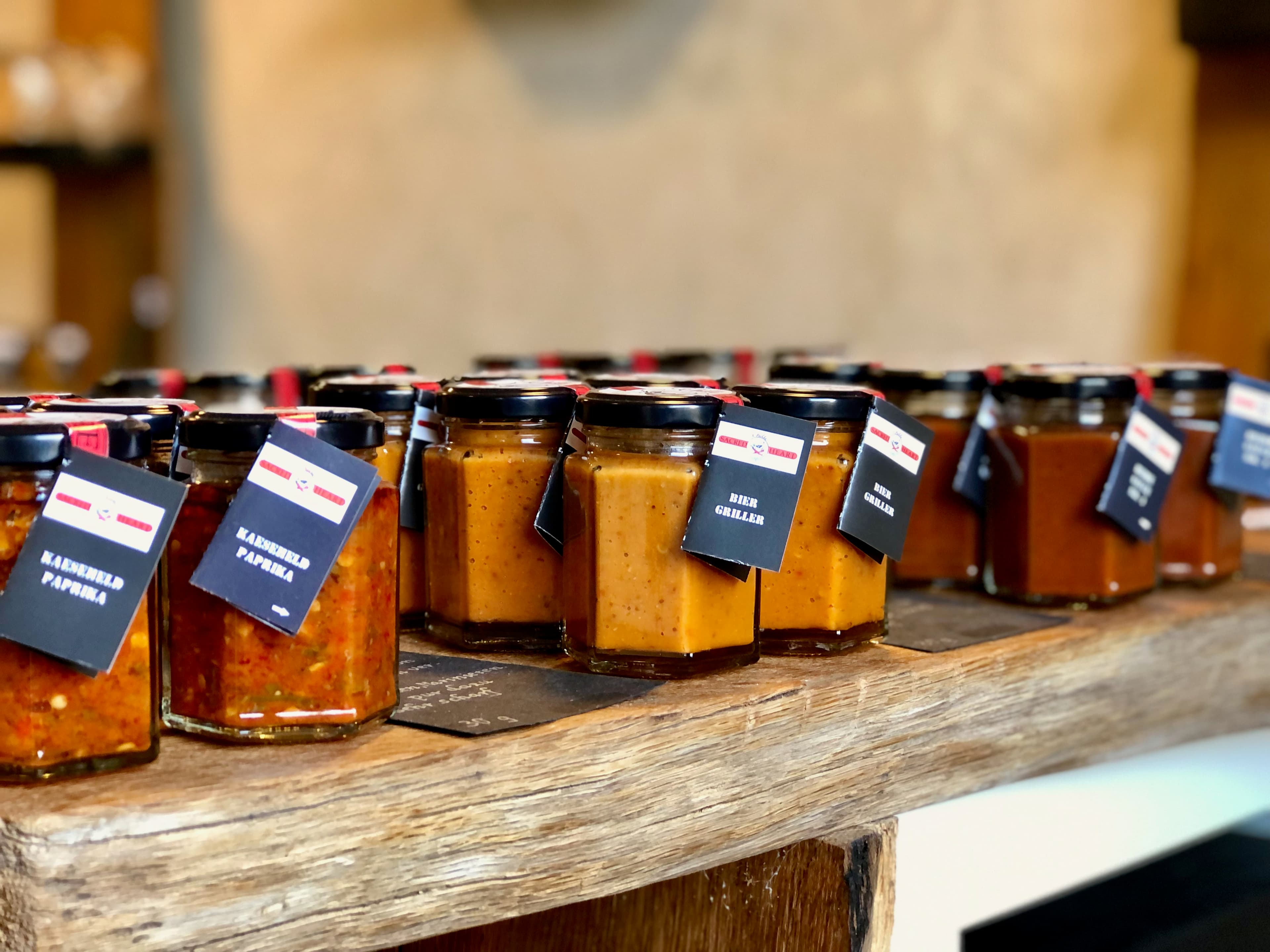 Das Bild zeigt Gläser mit herzhaften Saucen und Dips auf einem Eichentisch im Hofladen. In den Sorten Käseheld, Biergriller und Heidesauce No. 1 Chilli Manufaktur Susanne Menke Lüneburger Heide