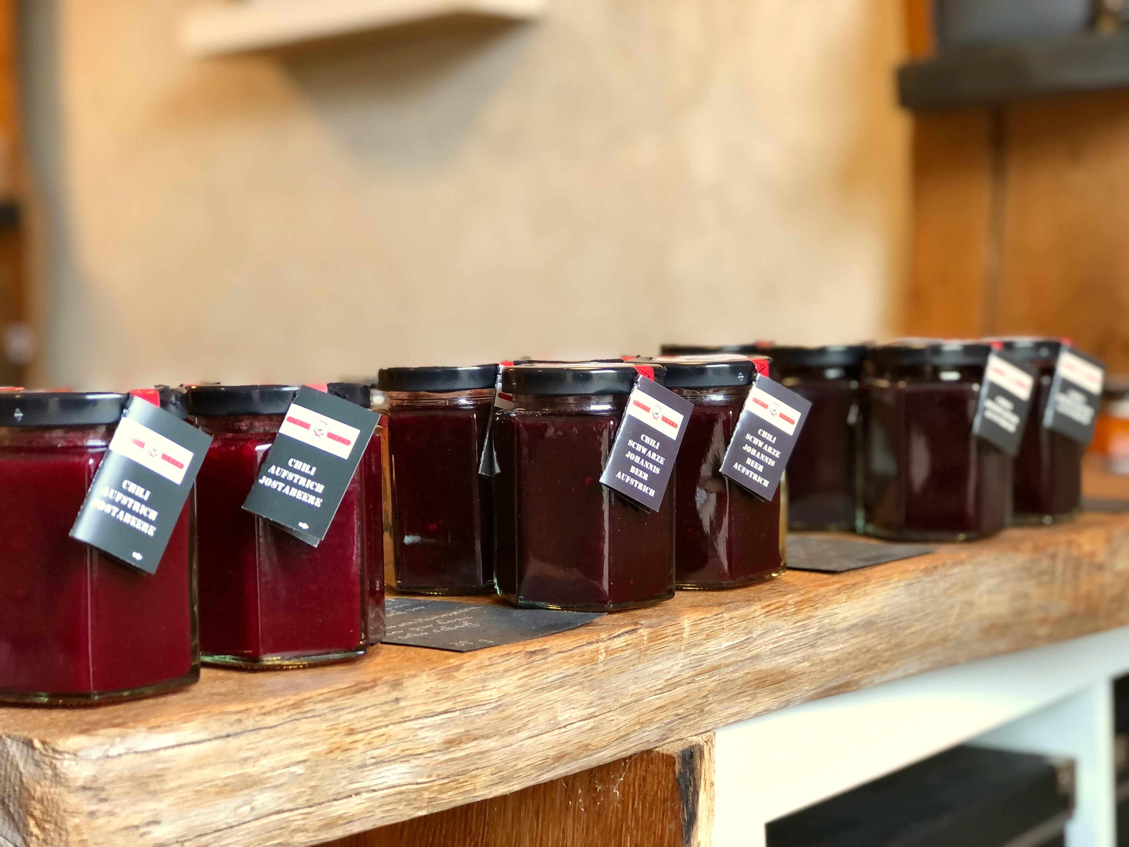 Das Bild zeigt exklusive Fruchtaufstriche mit Chili im Glas auf einem Eichentisch im Hofladen in den Sorten: Jostabeere, schwarze Johannisbeere und Heidelbeere Chilli Manufaktur Susanne Menke Lüneburger Heide
