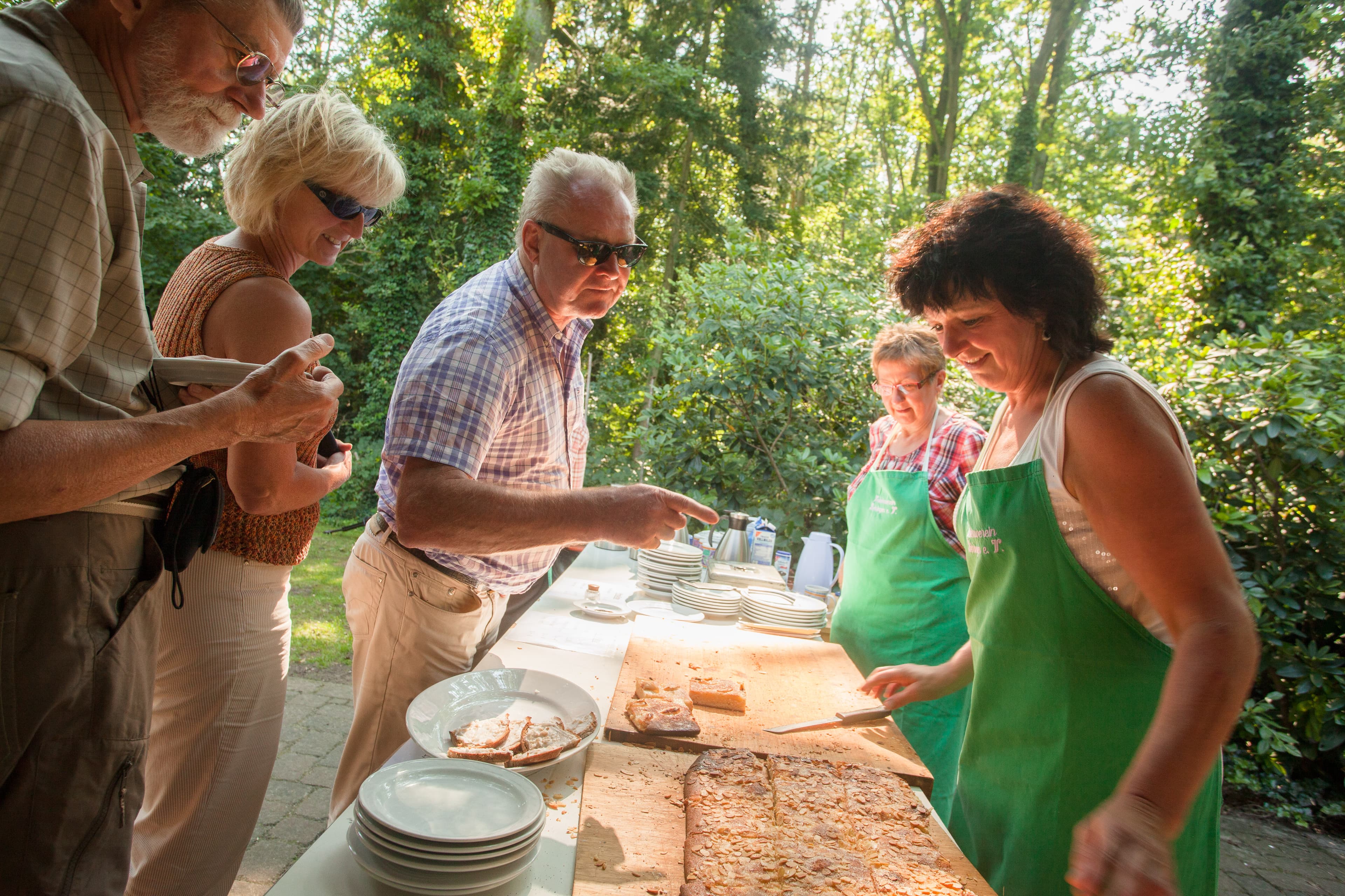 Menschen genießen im Freien frischen Butterkuchen, serviert von Frauen mit grünen Schürzen.