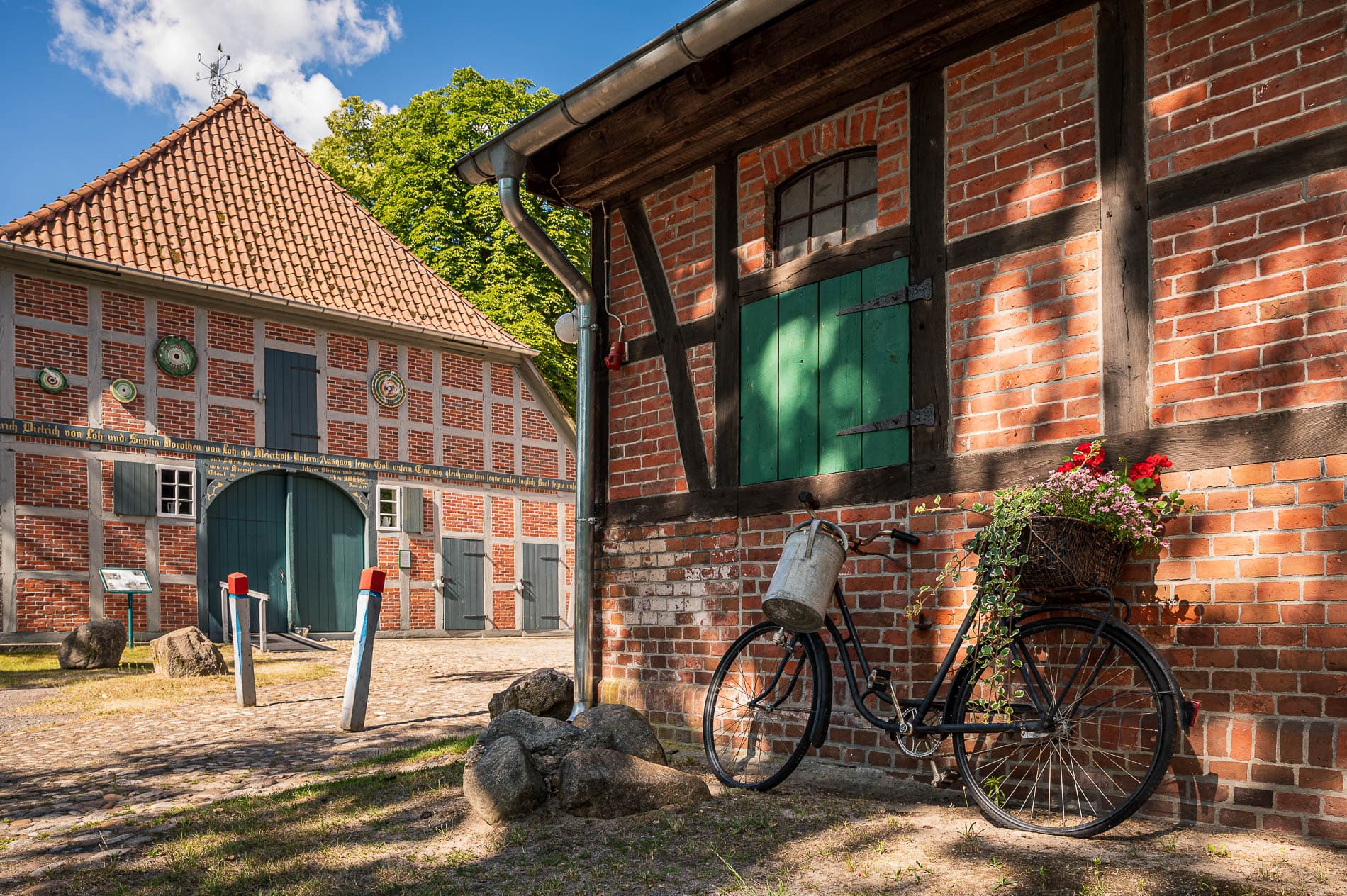 Fachwerkhäuser aus rotem Backstein, darunter ein Fahrrad mit einem Korb voller roter Blumen.