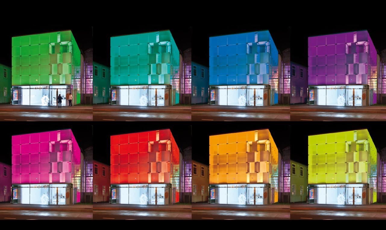 Collage mit acht Nachtaufnahmen des Glaskubus vom Kunstmuseum Celle; das Gebäude ist jeweils in einer anderen Farbe beleuchtet: grün, türkis, blau, violett, pink, rot, orange und gelb.