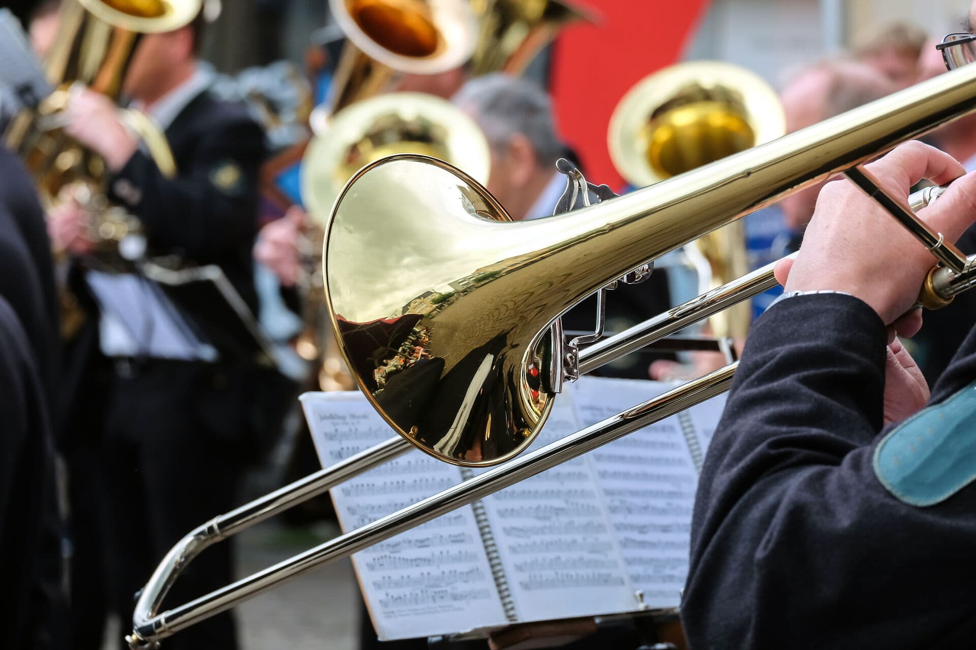 Ein Posaunenchor spielt im Freien, glänzende Instrumente reflektieren das Licht.A trombone choir plays outside, gleaming instruments reflecting the light.Et basunkor spiller udenfor, og de skinnende instrumenter reflekterer lyset.Een trombonekoor speelt buiten, glimmende instrumenten weerspiegelen het licht.
