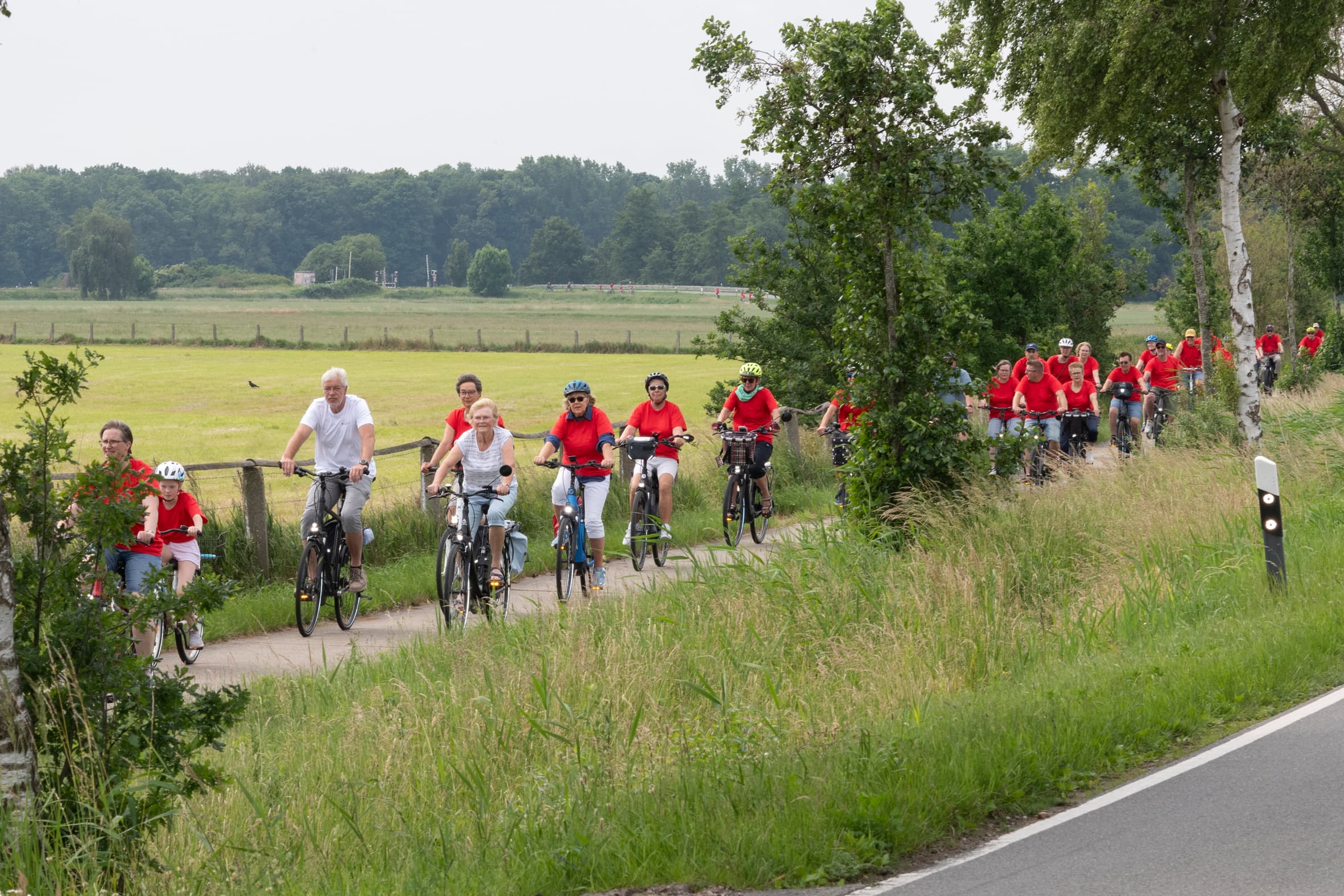 Teilnehmende der Tour de Marsch in roten Shirts auf FahrrädernTour de Marsch participants in red shirts on bicyclesTour de Marsch-deltagere i røde skjorter på cyklerTour de Marsch deelnemers in rode shirts op de fiets