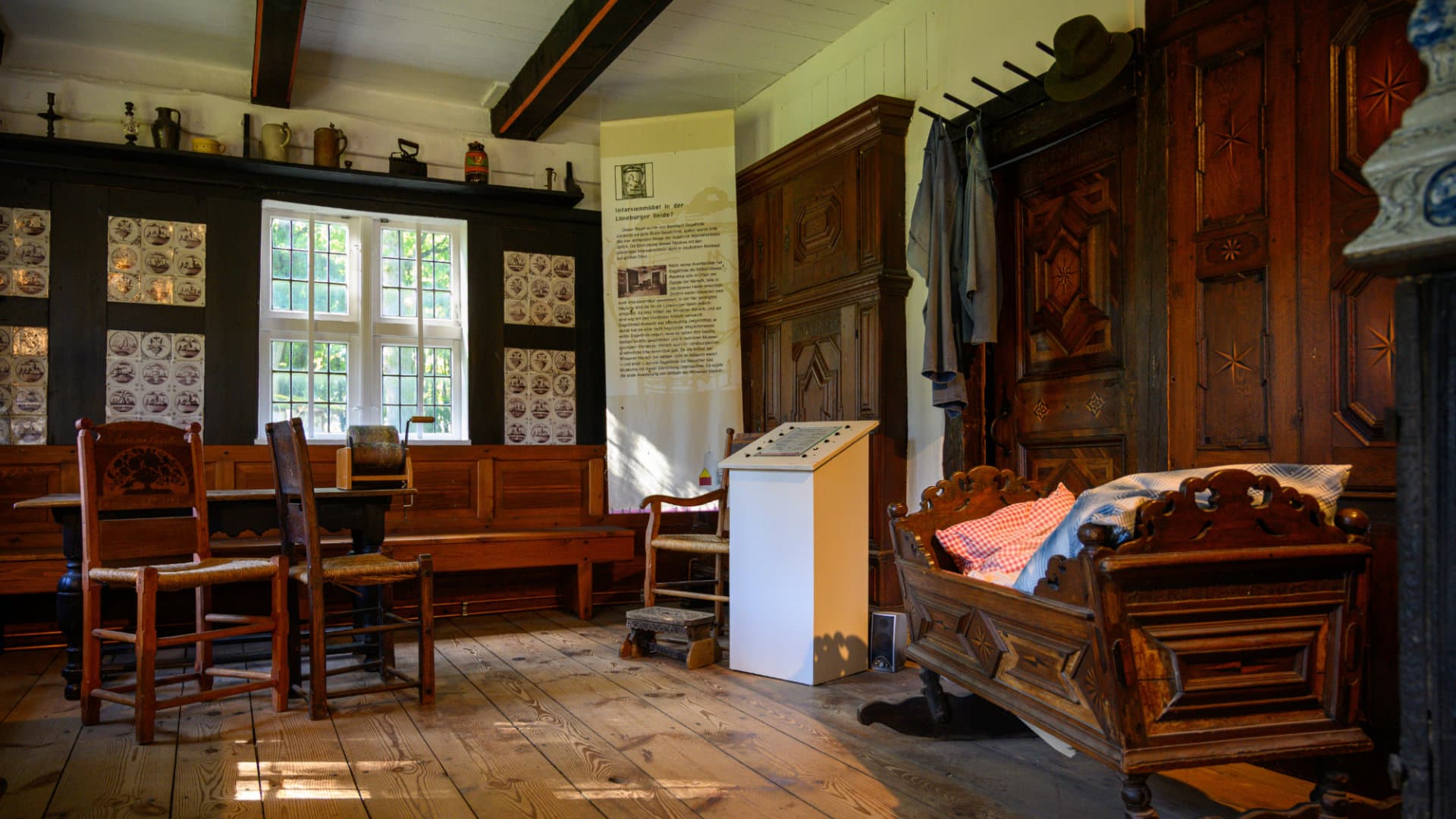 Museumzimmer mit Holzmöbeln, Wiege, Tisch, Stühlen und Kachelwand in historischem Bauernhaus.