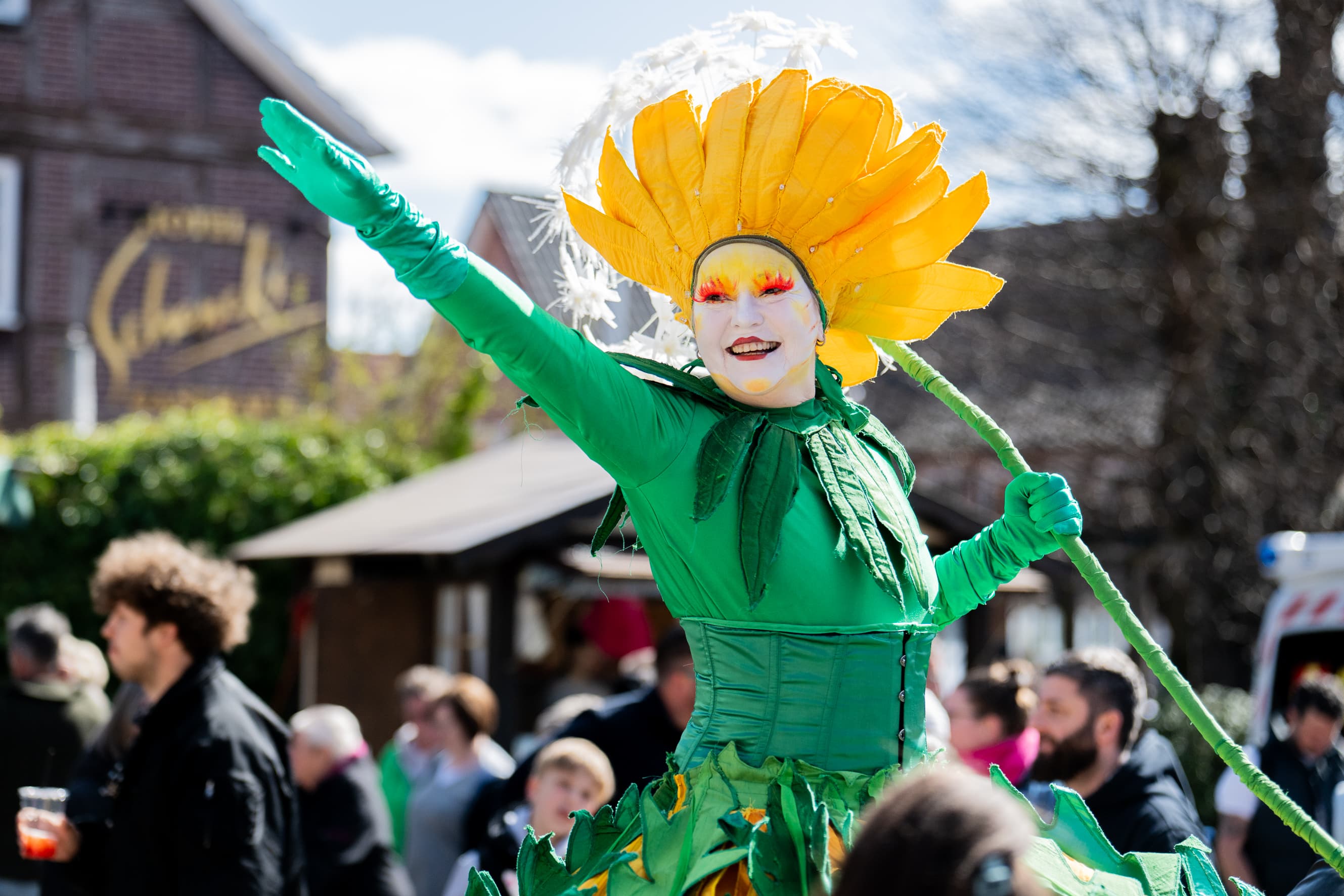 Bunter Walkact als Löwenzahn verkleidet winkt fröhlich auf dem Frühlingsmarkt in Amelinghausen.