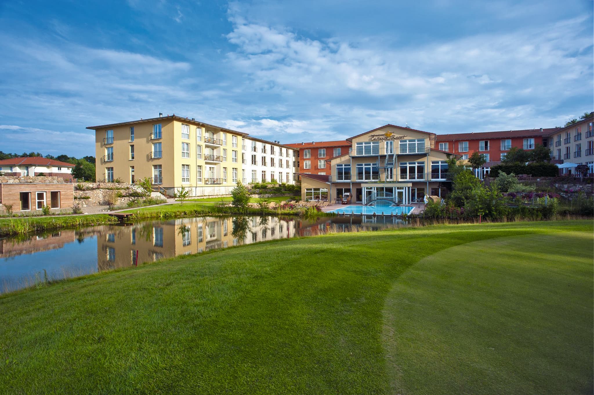 Außenansicht des Castanea Resorts mit großem Golfplatz, Teich und Poolanlage an einem sonnigen Tag.