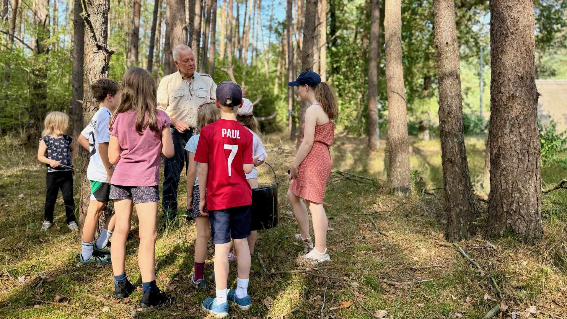 Kinder stehen im Wald und lauschen aufmerksam den Erklärungen eines Naturführers.