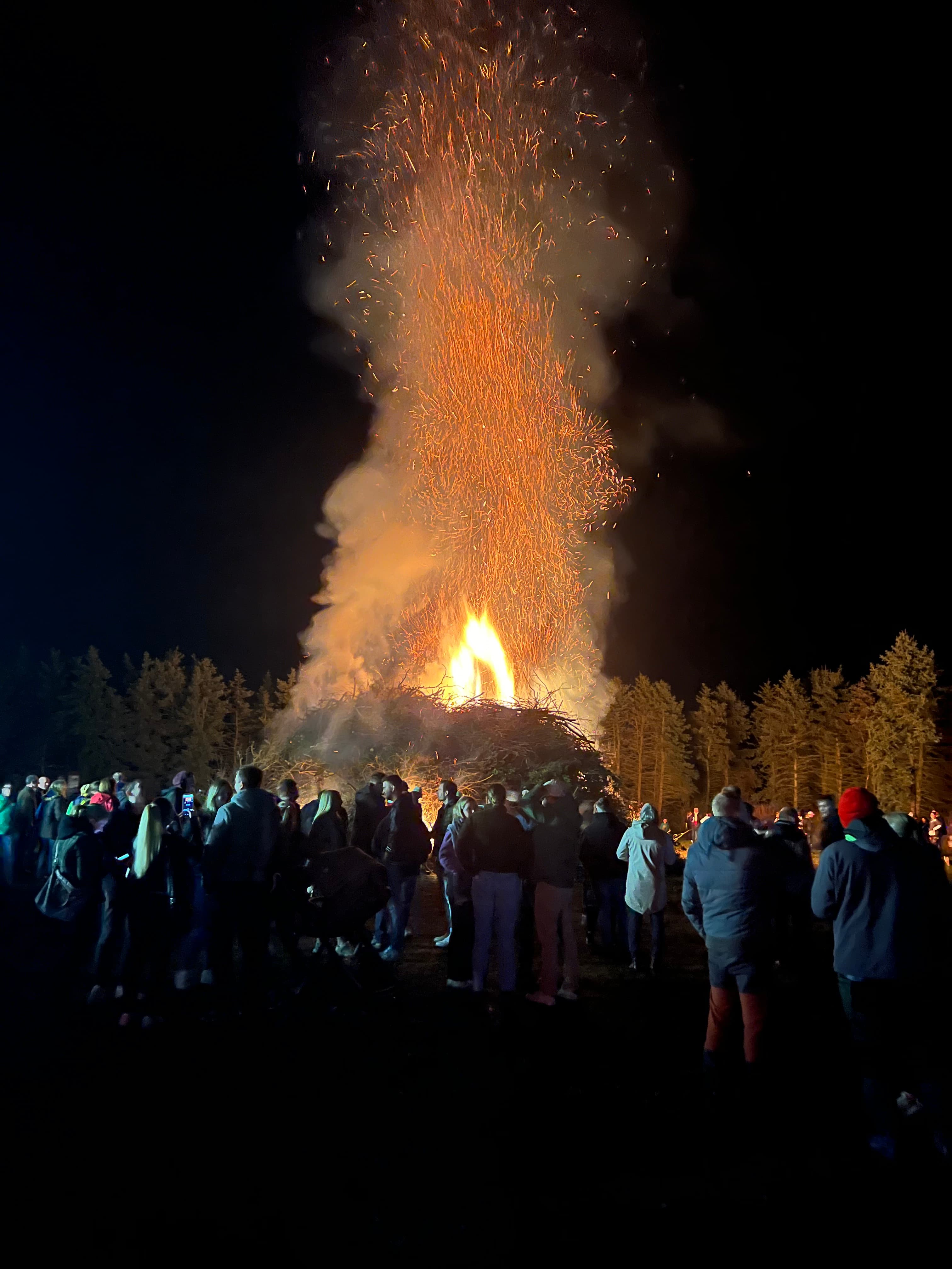 Ein riesiges Osterfeuer leuchtet in der Nacht, während eine Menschenmenge das Flammenspektakel beobachtet.