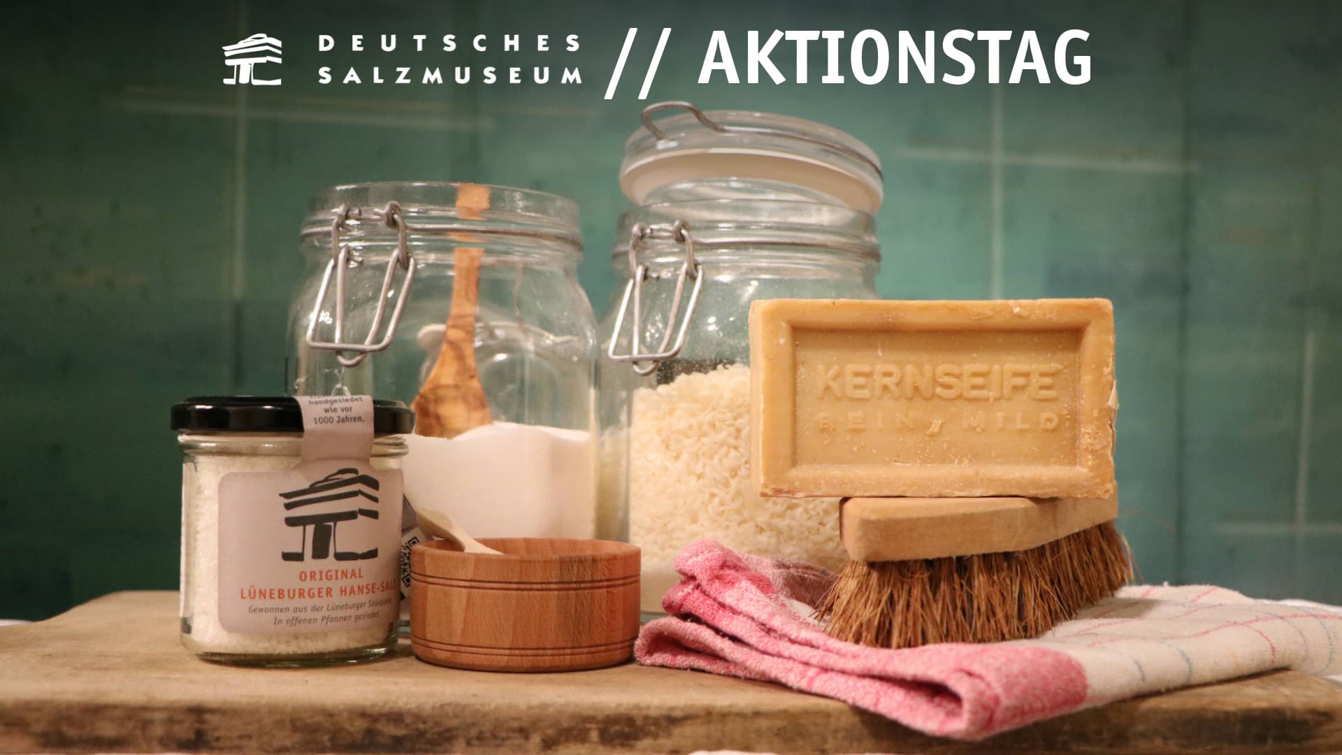 Verschiedene selbsthergestellte Waschmittel, Kernseife, Salz und Putzutensilien stehen auf einem Tisch.