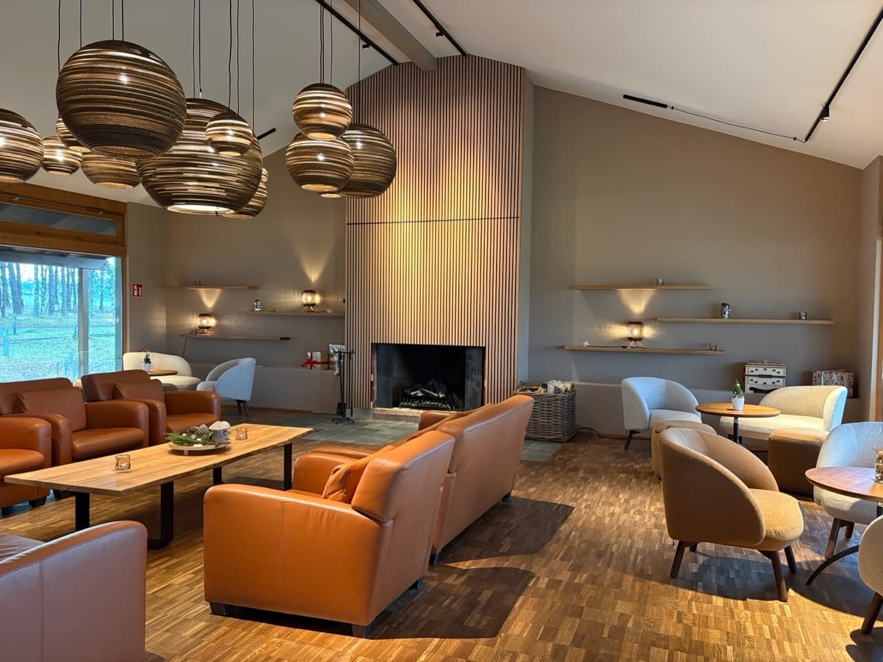 Ein großer Raum mit Kamin. Es gibt braune Sessel. Oben hängen runde Lampen.