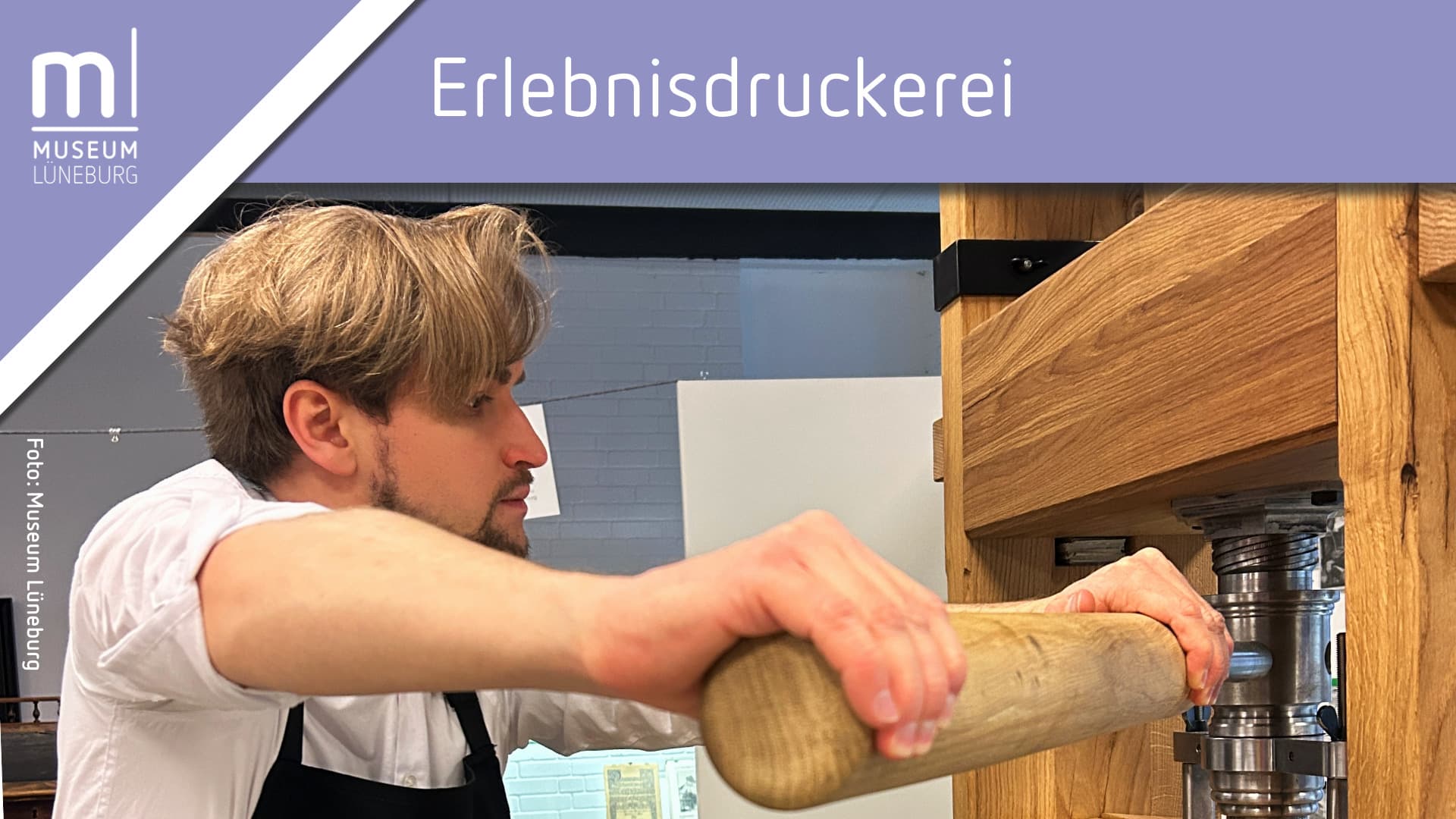 Ein Mann steht an der Druckerpresse und drückt einen Hebel aus Holz.