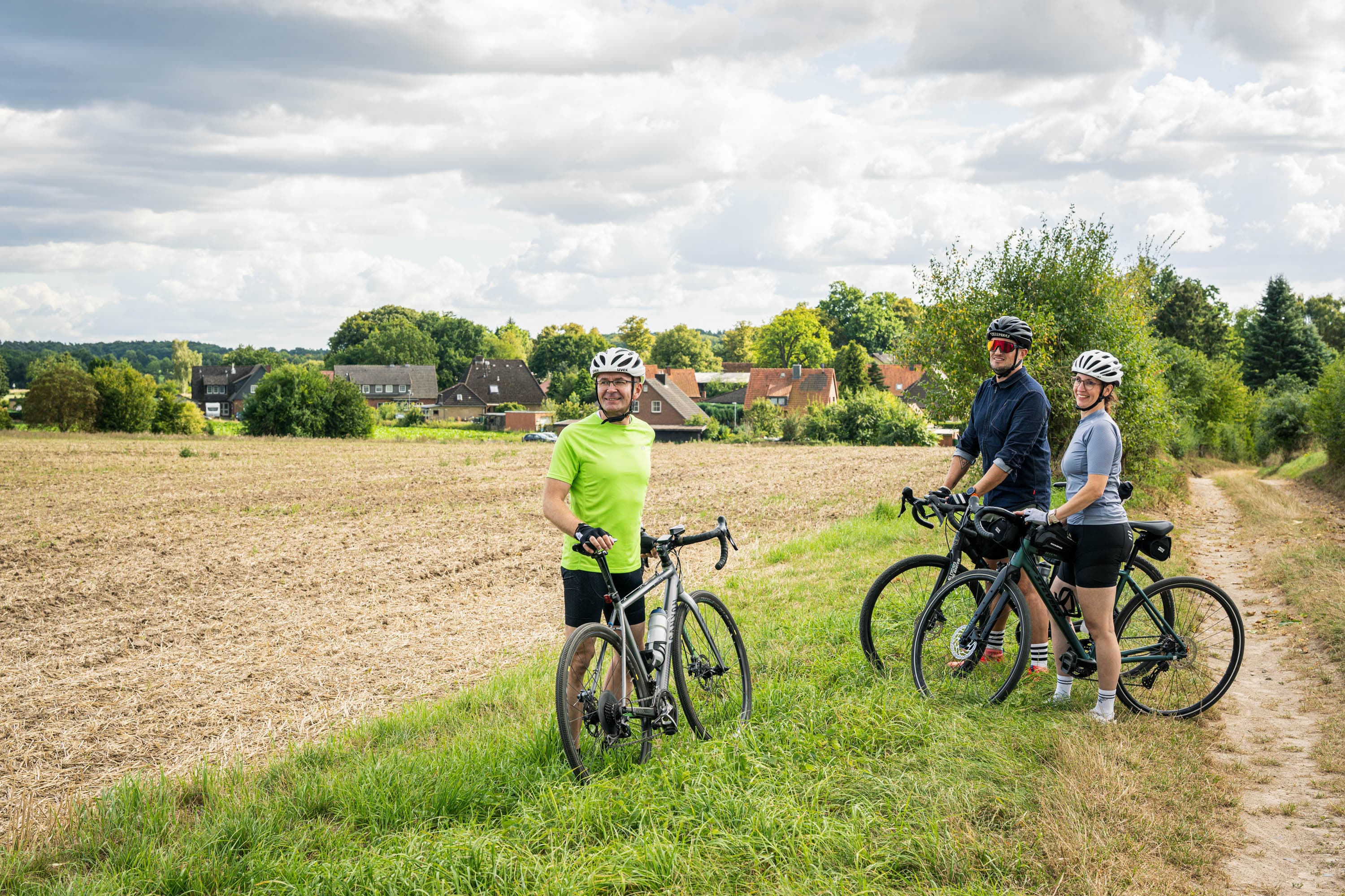 Gravelbiker am Feldrand mit schöner Sicht auf ländliche Landschaft mit einem Dorf im Hintergrund