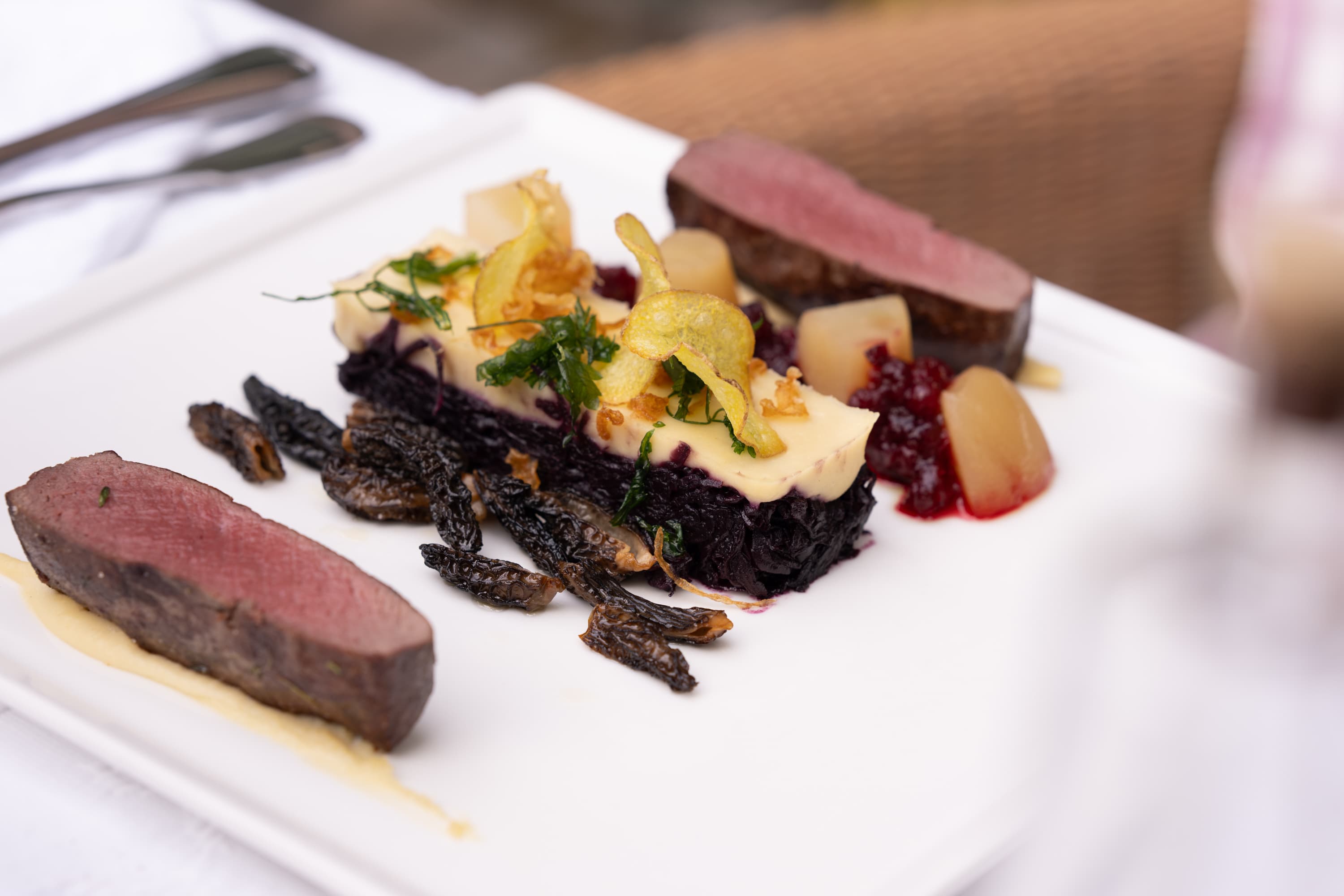 Rosa gebratenes Heidschnuckenfilet mit Rotkohl und Morcheln auf einem weißen Teller angerichtet.