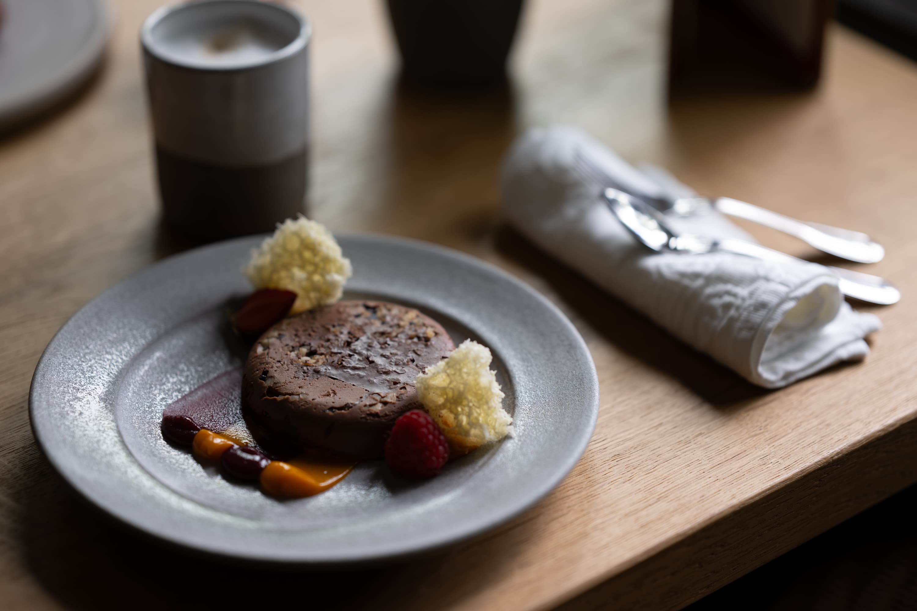 Ein Schokoladendessert, angerichtet mit frischen Beeren und Soße auf einem grauen Keramikteller.