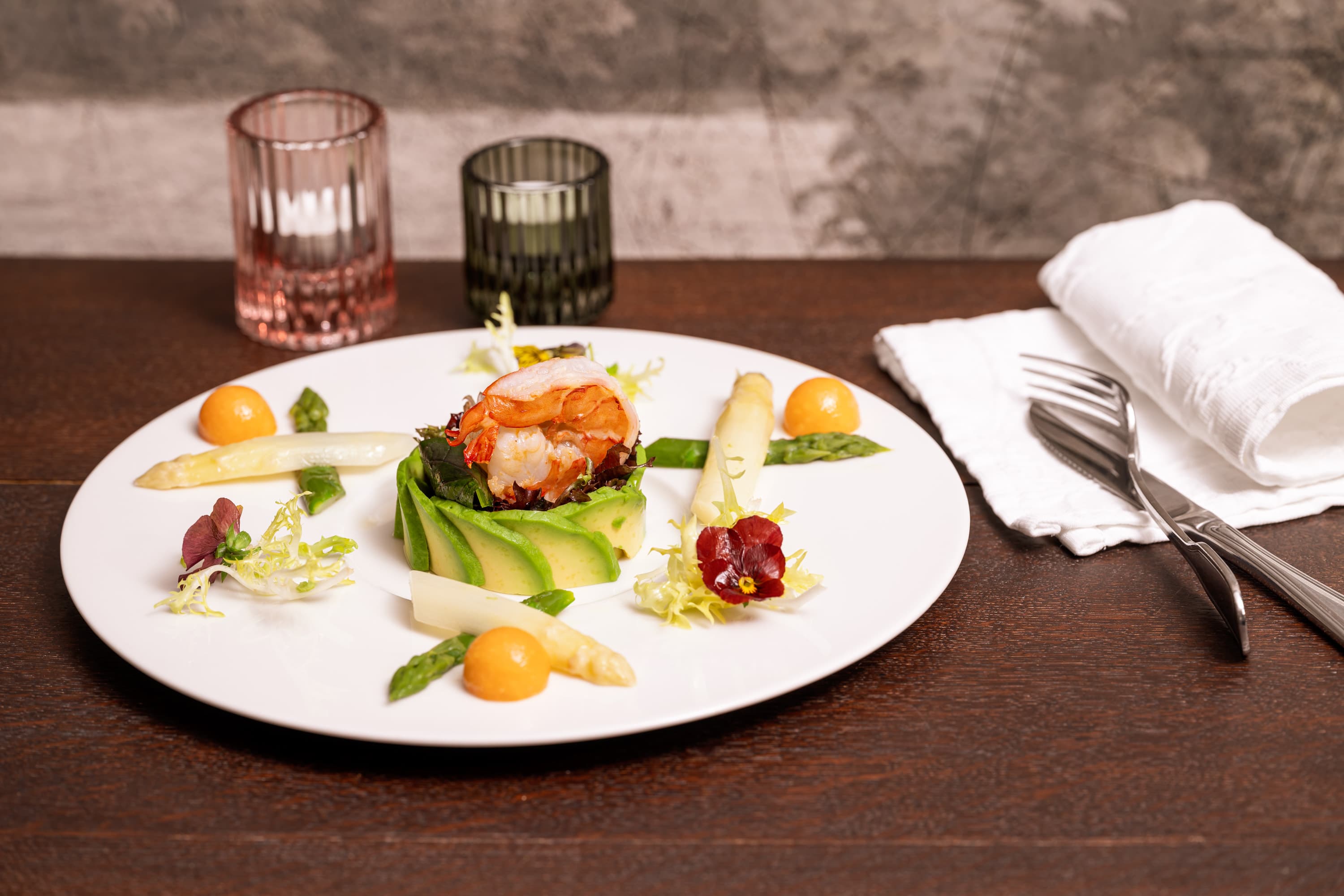 Kunstvoll angerichtete Vorspeise: Garnele auf Avocadosalat mit Spargel und essbarer Blüte.