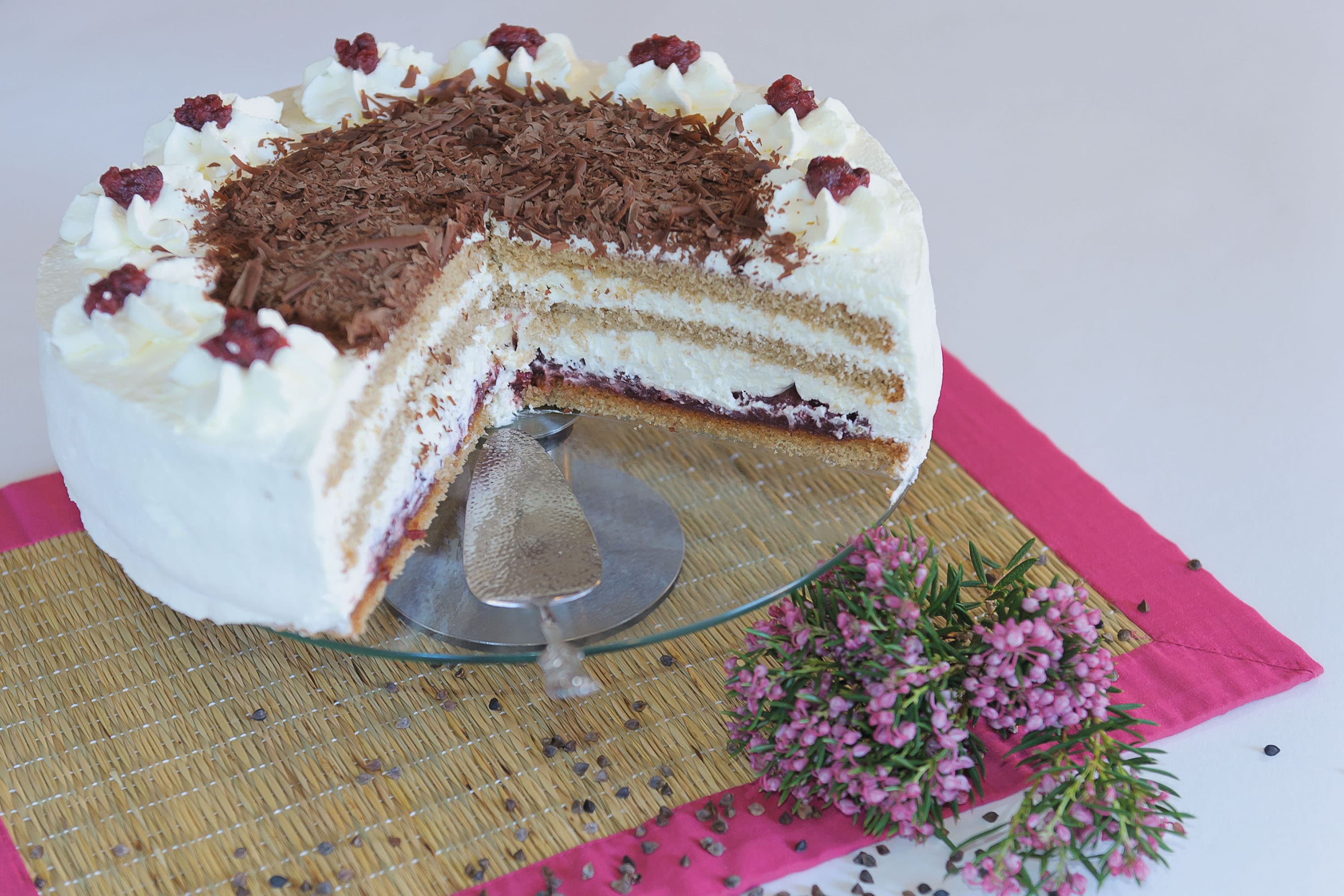 Angeschnittene Buchweizentorte mit Sahne und Schokoraspeln, dekoriert mit Heidekraut.