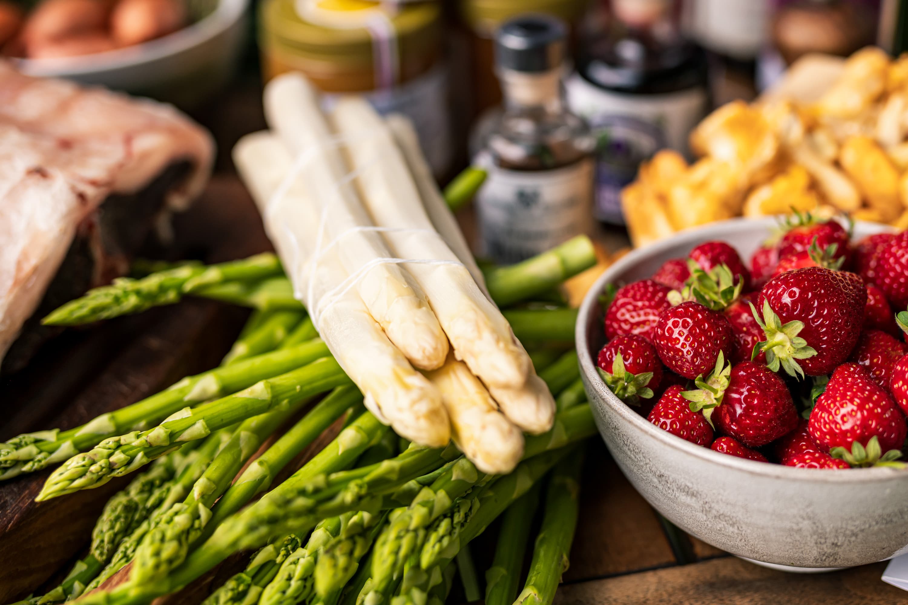 Frischer weißer Spargel auf grünem Spargel, daneben eine Schale Erdbeeren und Pfifferlinge.