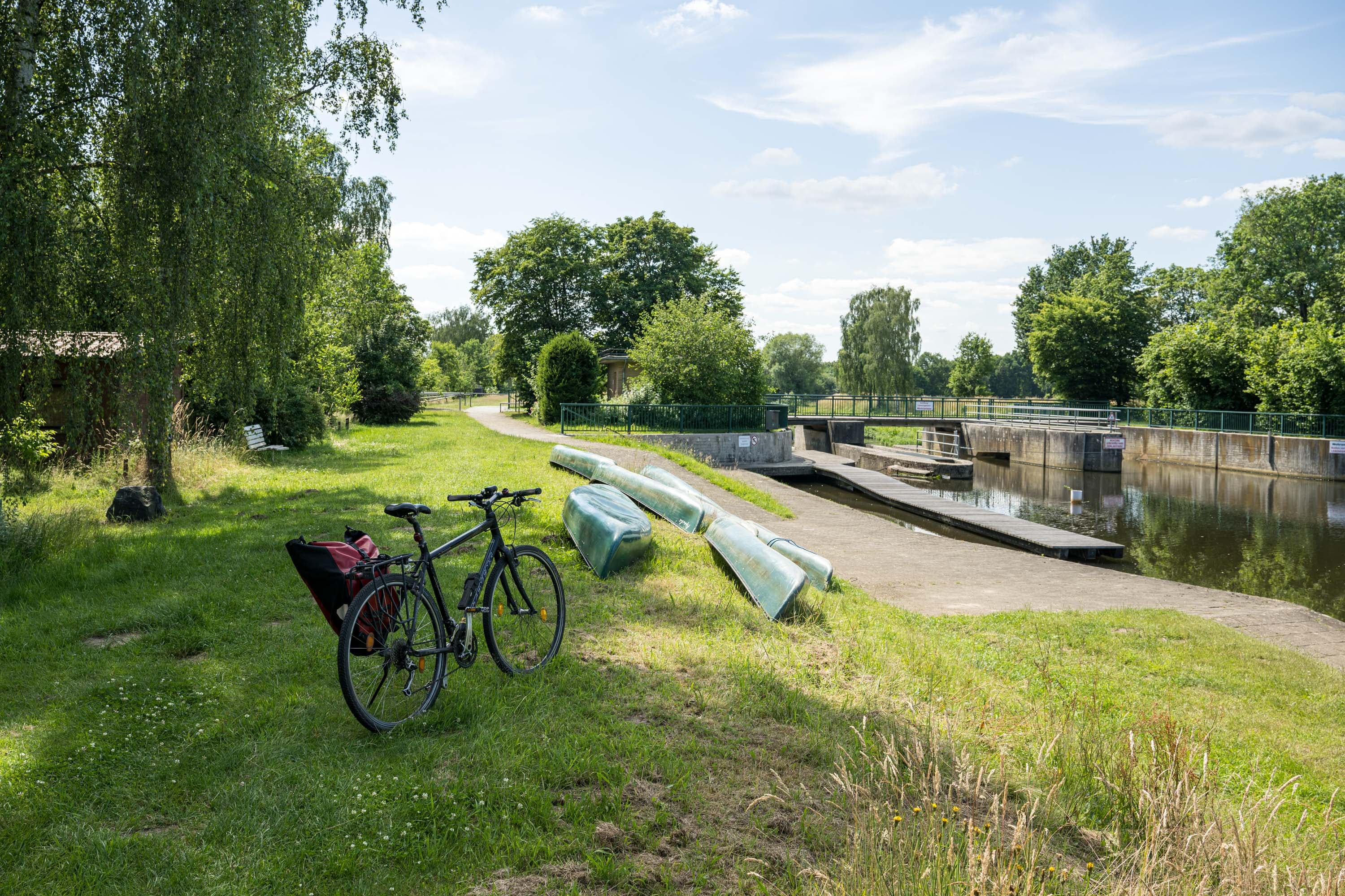 Fahrrad am Aller-Radweg neben Kanus und Schleuse am grünen Allerufer