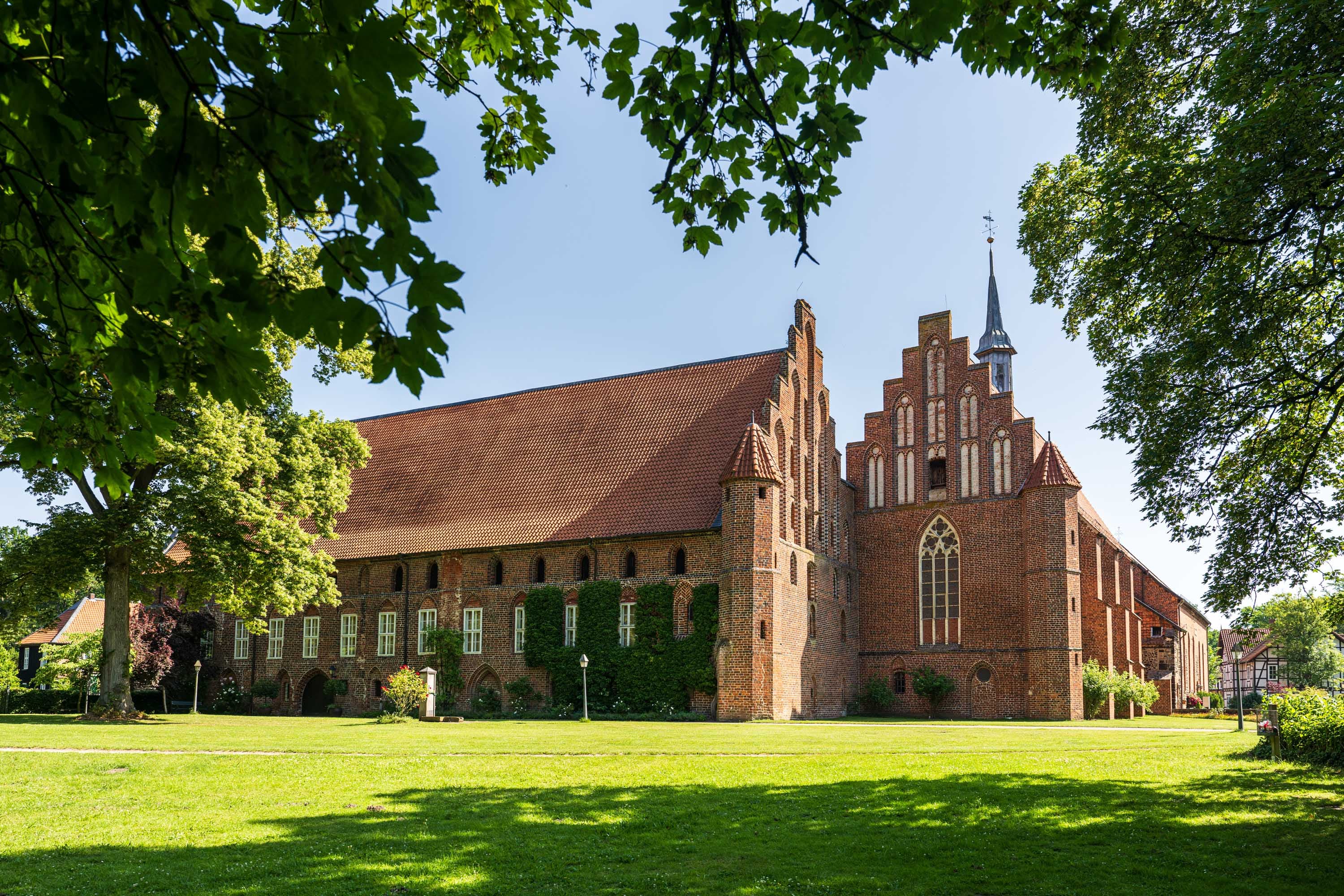 Backsteinkloster Wienhausen mit rotem Dach, Wiese und alten Bäumen im Sonnenlicht