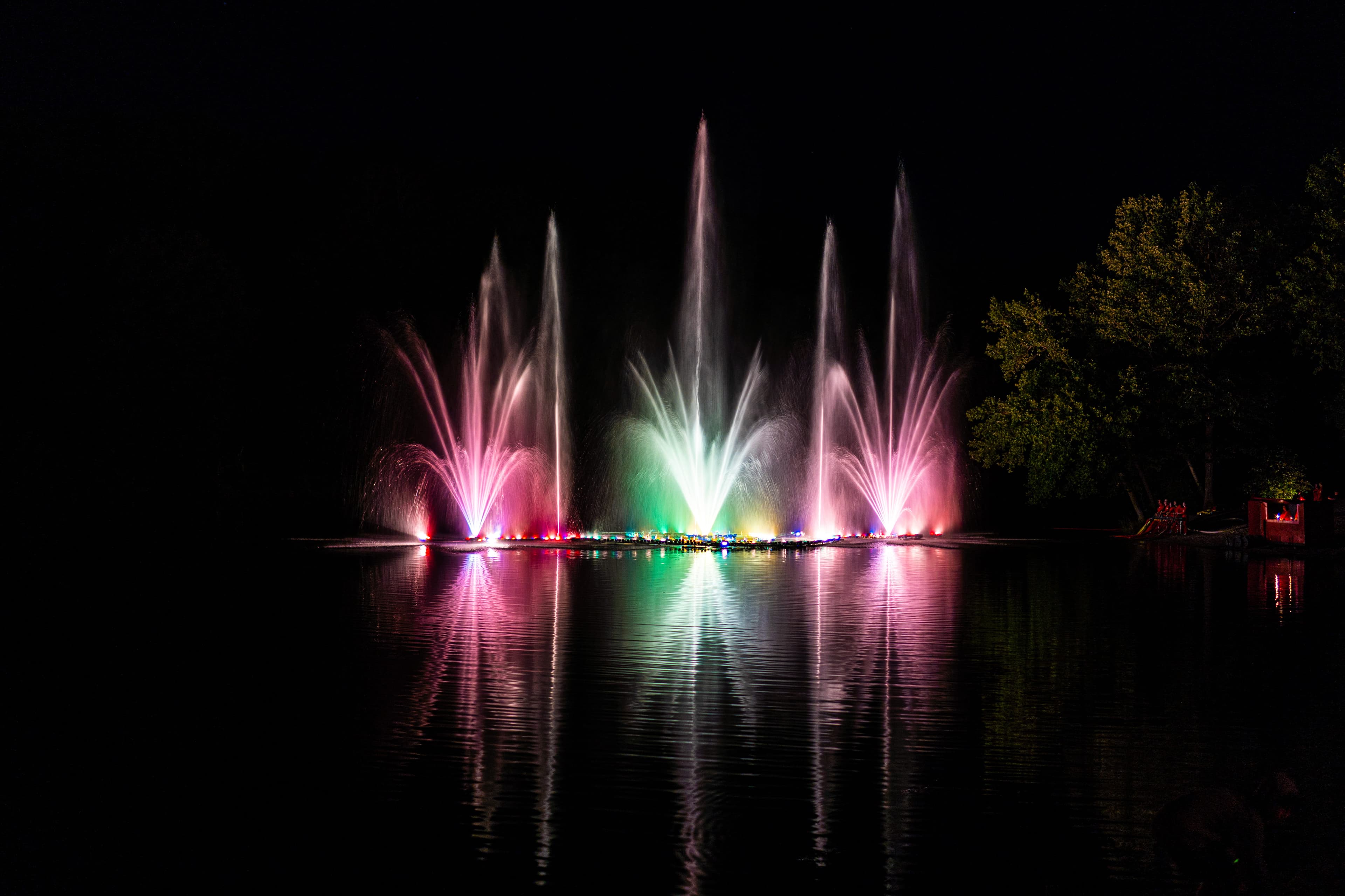 Bunte Wasserfontänen leuchten nachts über dem Brunausee in Behringen und spiegeln sich im Wasser.