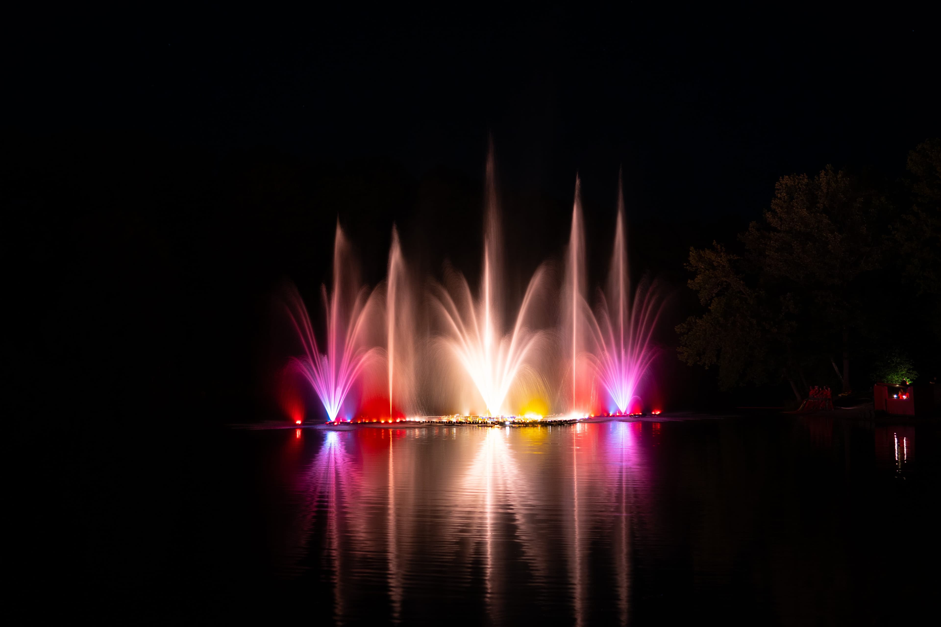 Bunte Wasserfontänen mit Lichteffekten spiegeln sich nachts im Brunausee in Behringen..