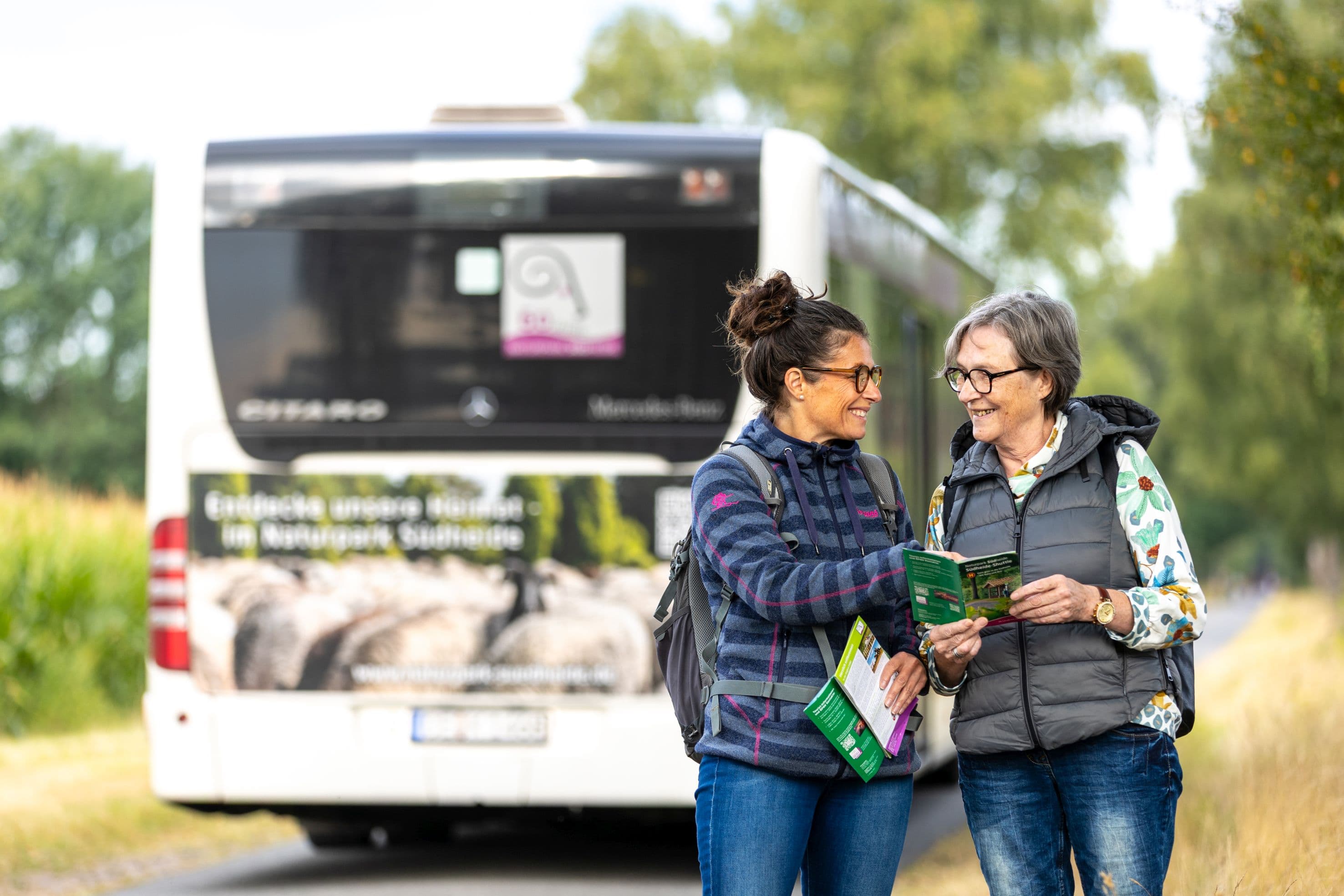 zwei frauen stehen vor einem bus mit einer wanderkarte in der hand