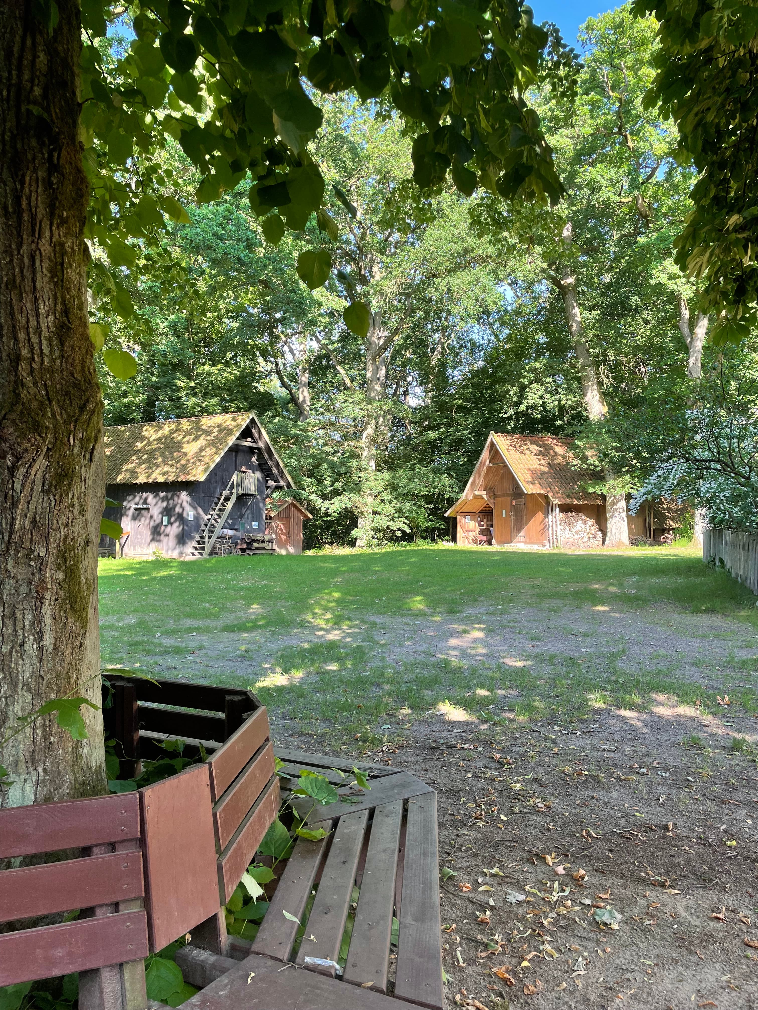 Historischer Treppenspeicher auf einer schattigen Wiese unter alten Bäumen.