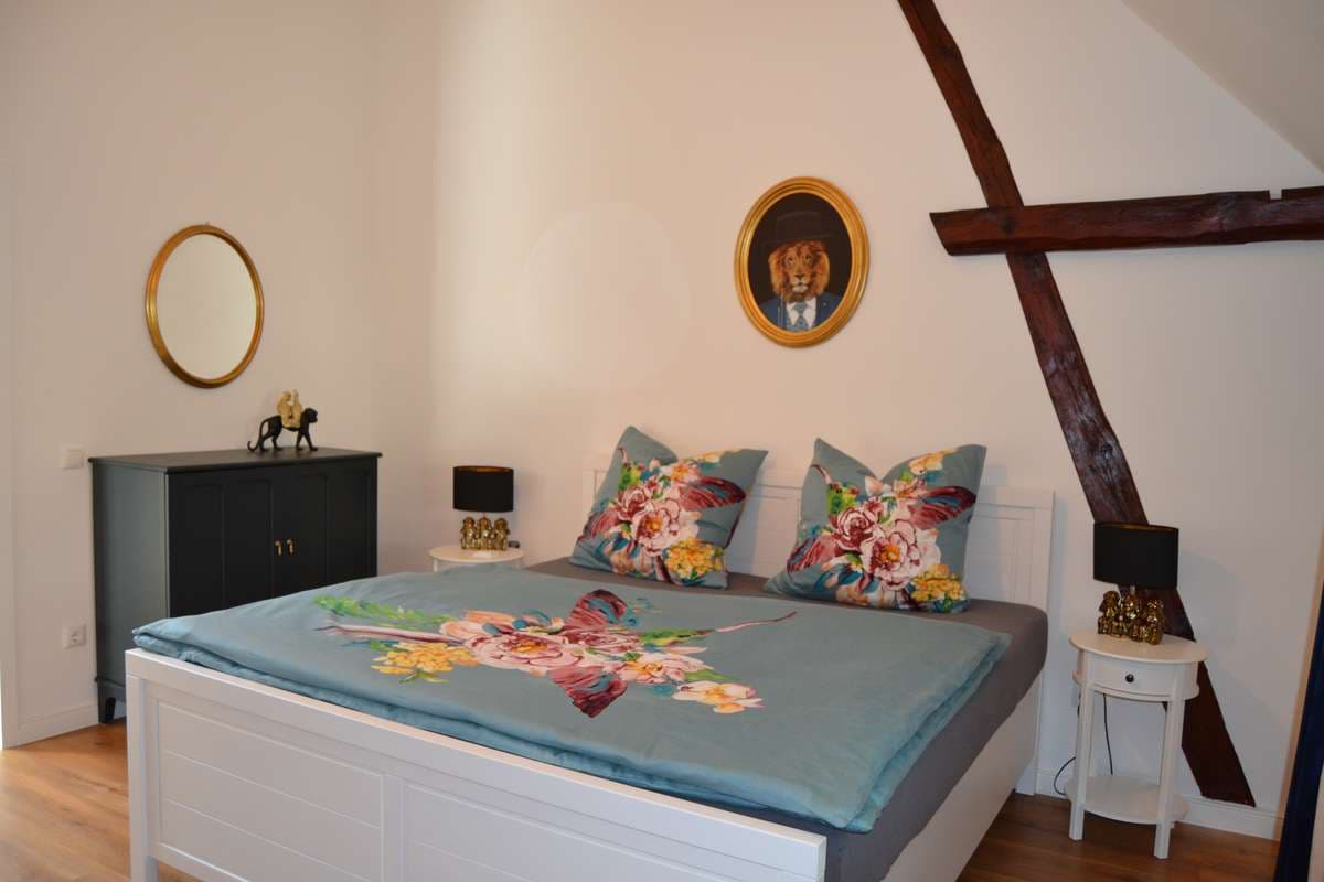 Löwenzimmer mit Doppelbett, türkiser Blumenbettwäsche und Löwenporträt an der Wand