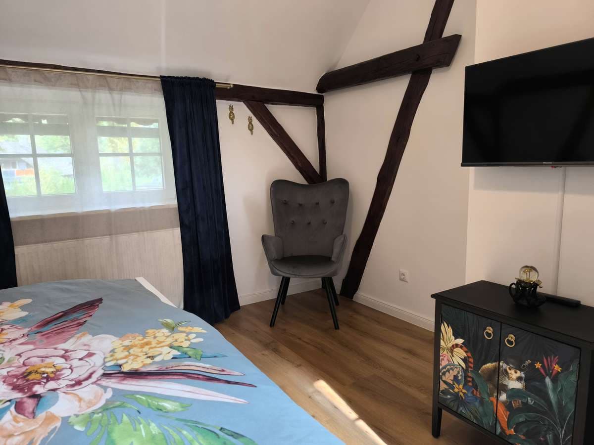 Löwenzimmer mit türkiser Bettwäsche, Sessel, Fernseher und bemalter Kommode