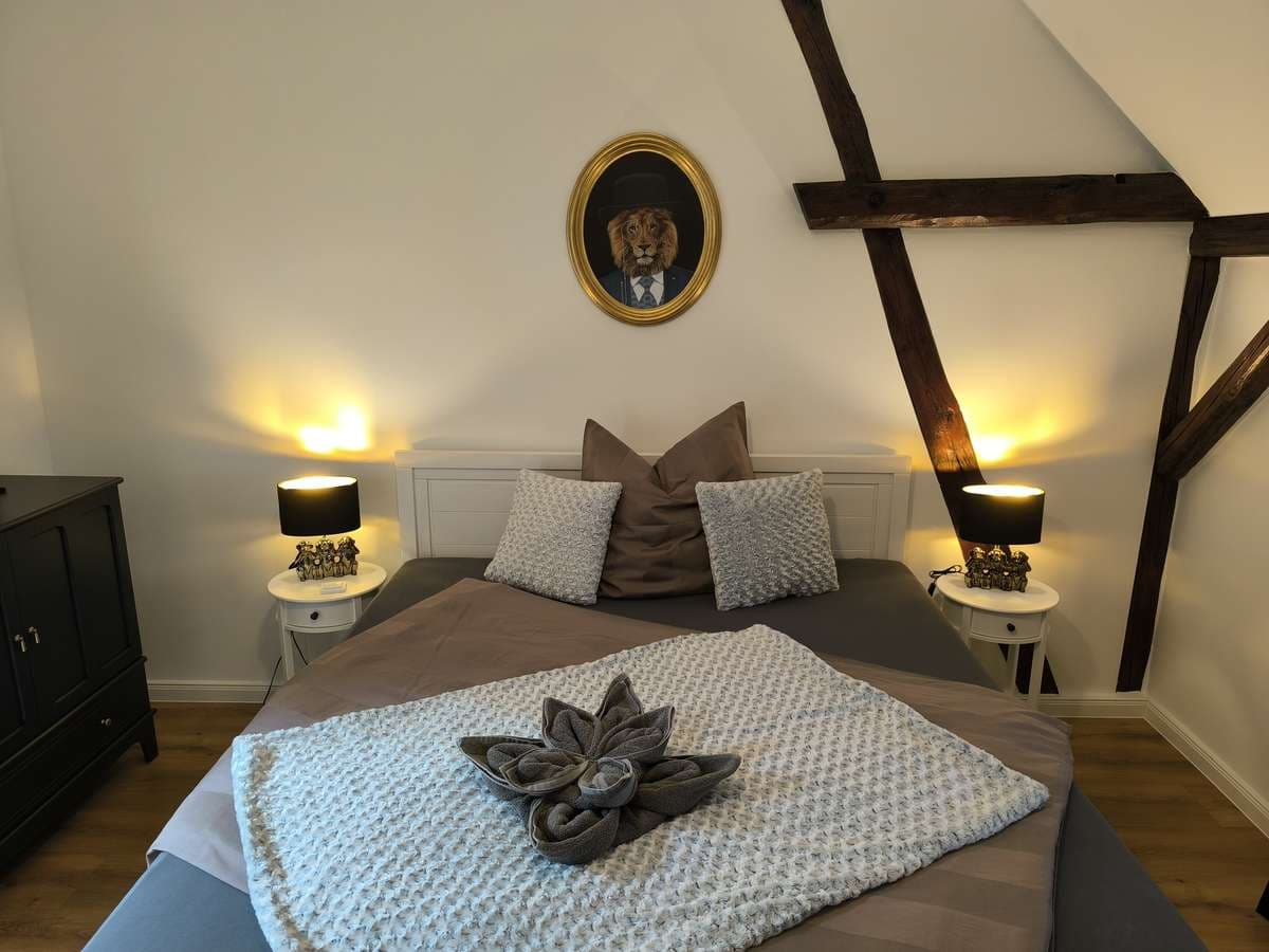 Doppelbett mit grau-beiger Bettwäsche, Handtuchblume und Löwenporträt