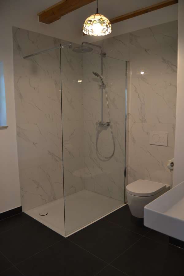 Bodengleiche Dusche in Marmoroptik mit Regendusche, Glaswand und Wand-WC unter Holzbalkendecke